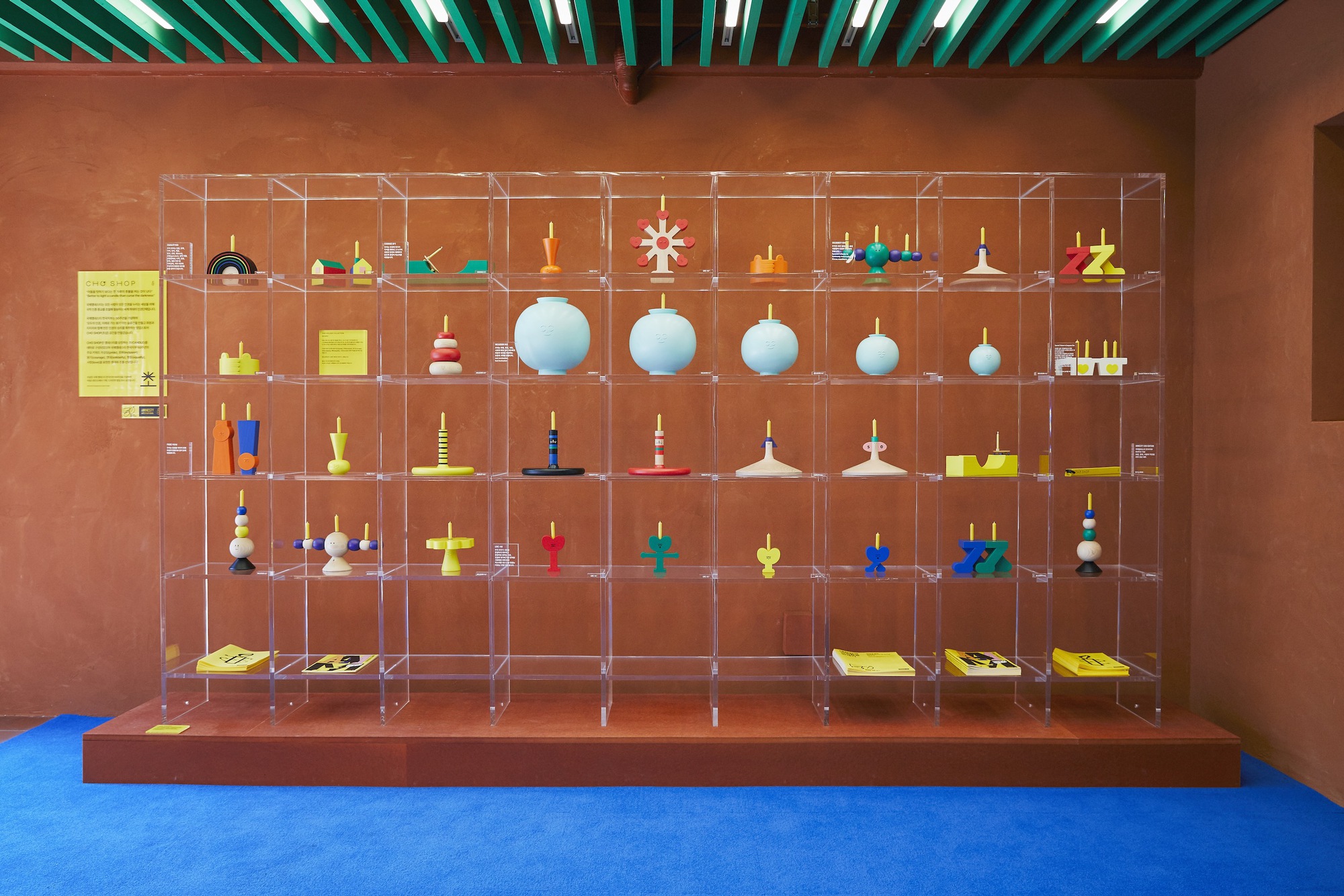 Grid of transparent shelving units displaying toy collection beneath green linear ceiling lights