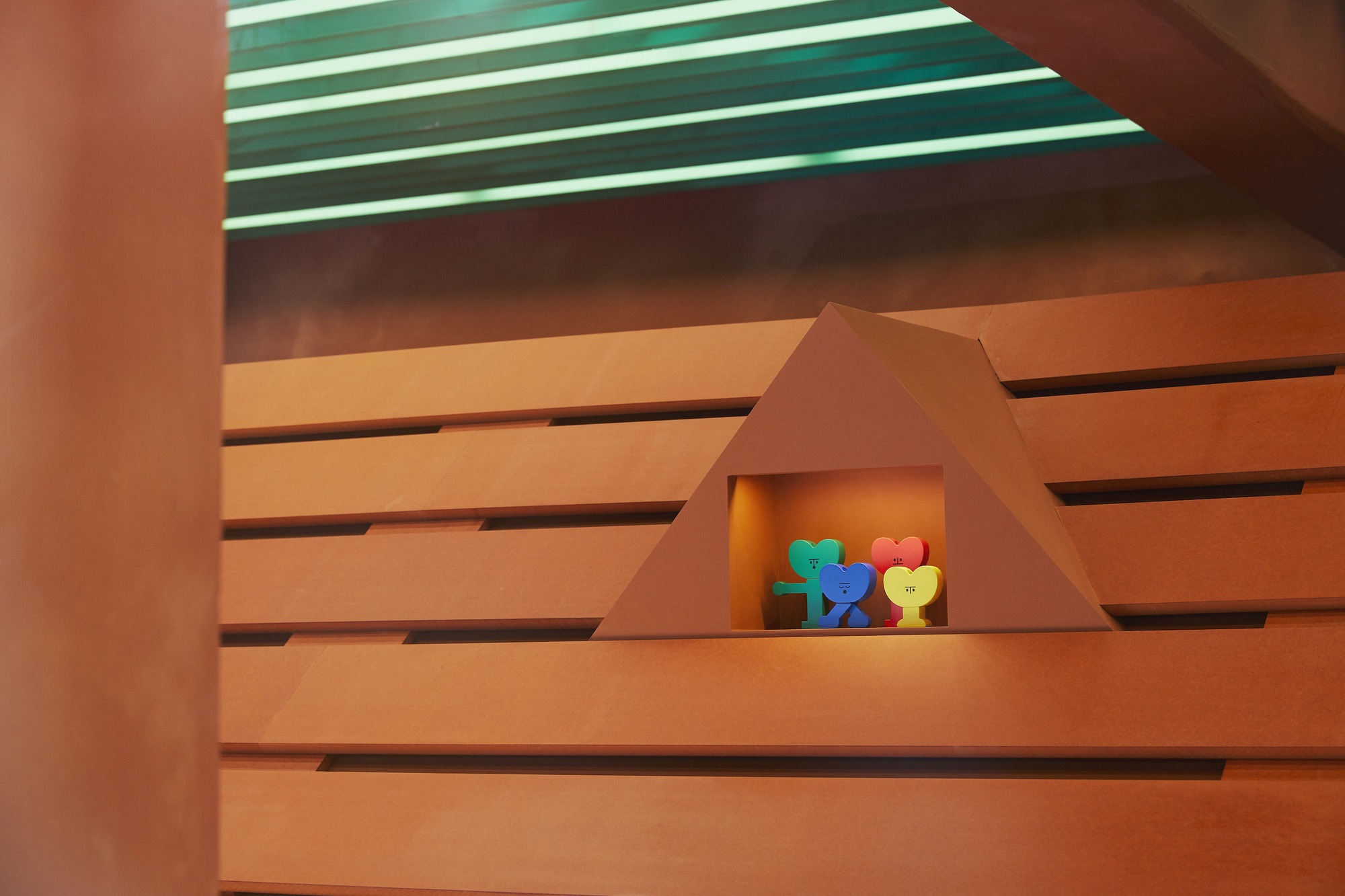 Triangular recess in horizontal wood slat wall with colorful objects under green striped ceiling