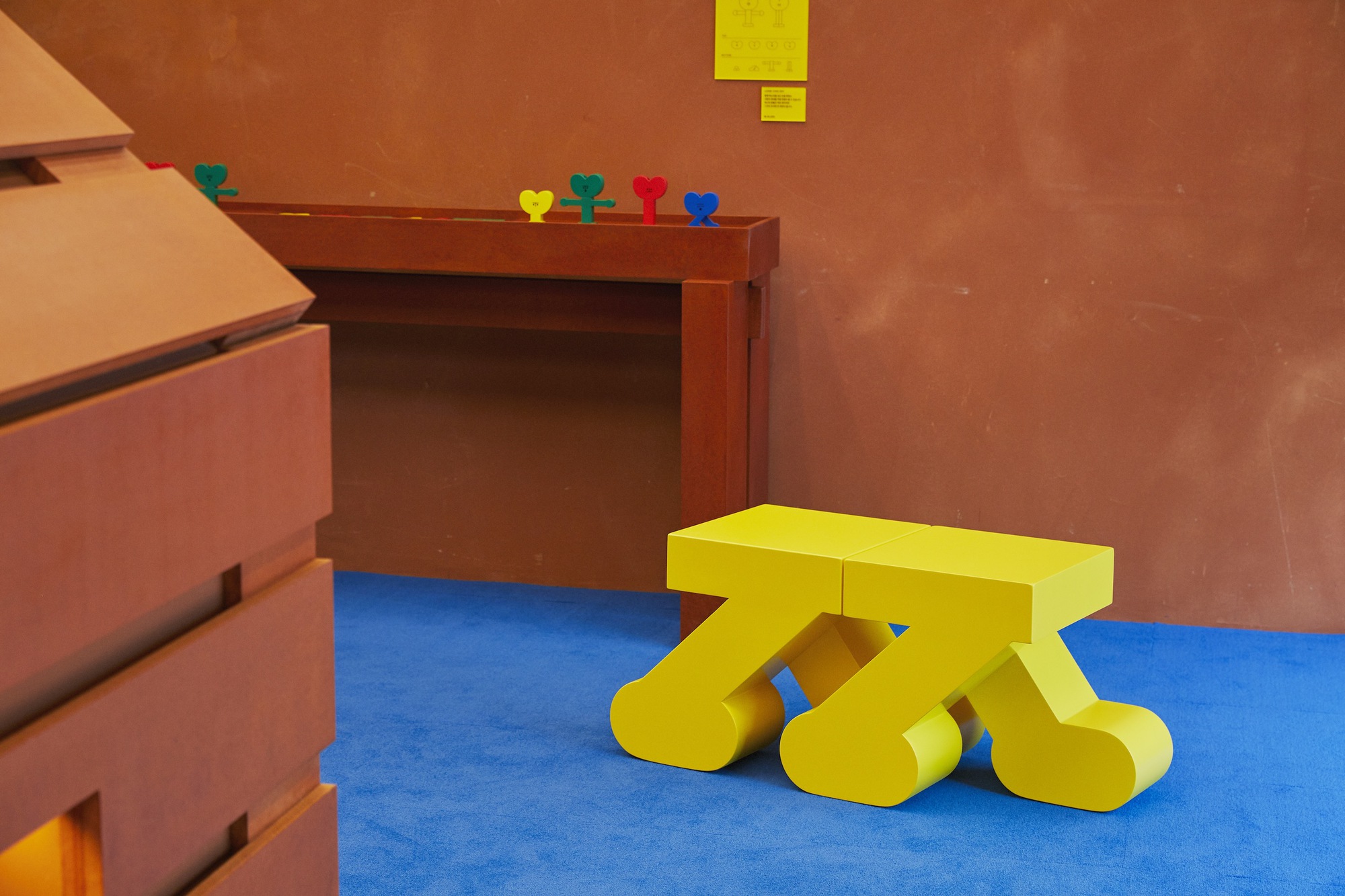 Yellow sculptural bench on blue flooring beside terracotta walls and timber built-in furniture