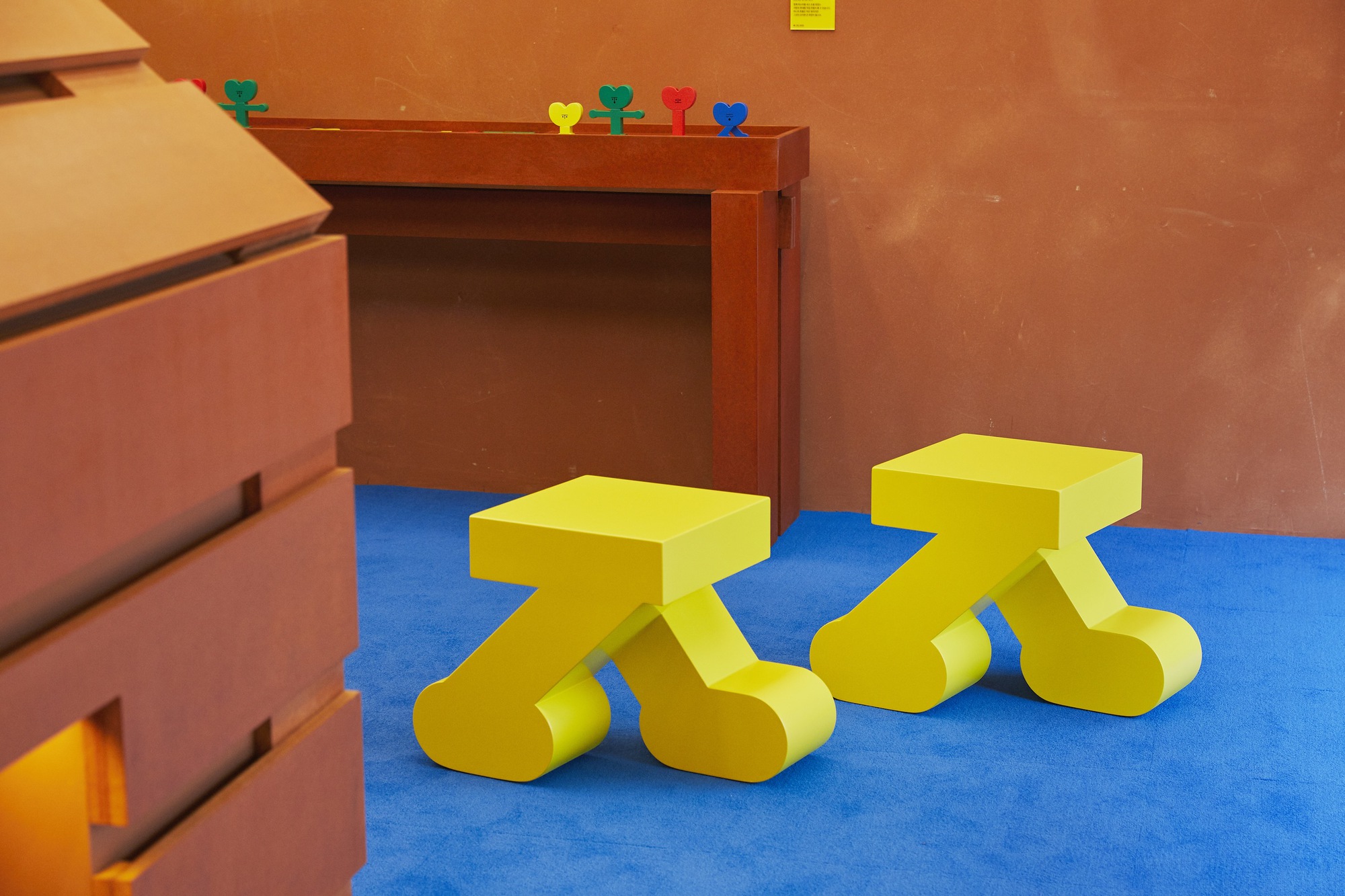 Two yellow stools with curved legs on blue flooring near timber cabinetry and terracotta walls