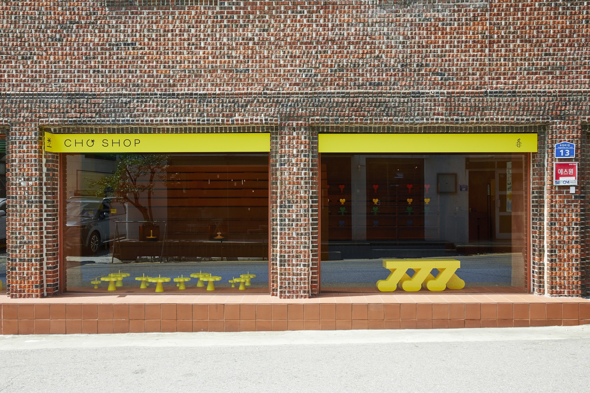 Street facade with patterned brickwork and full-height glazing beneath yellow signage bands