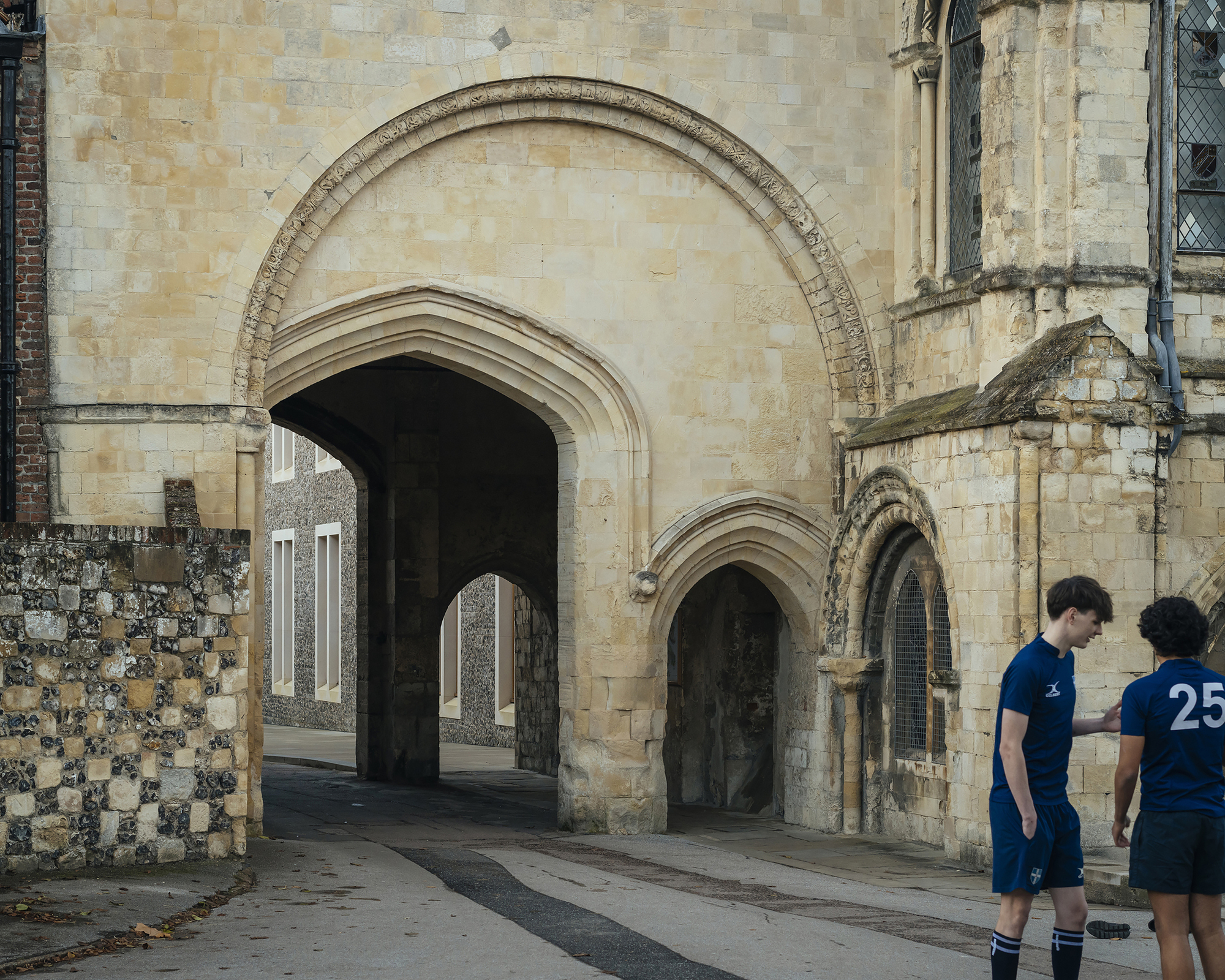 Stone arched gateway framing a view of the flint facade with two students standing outside