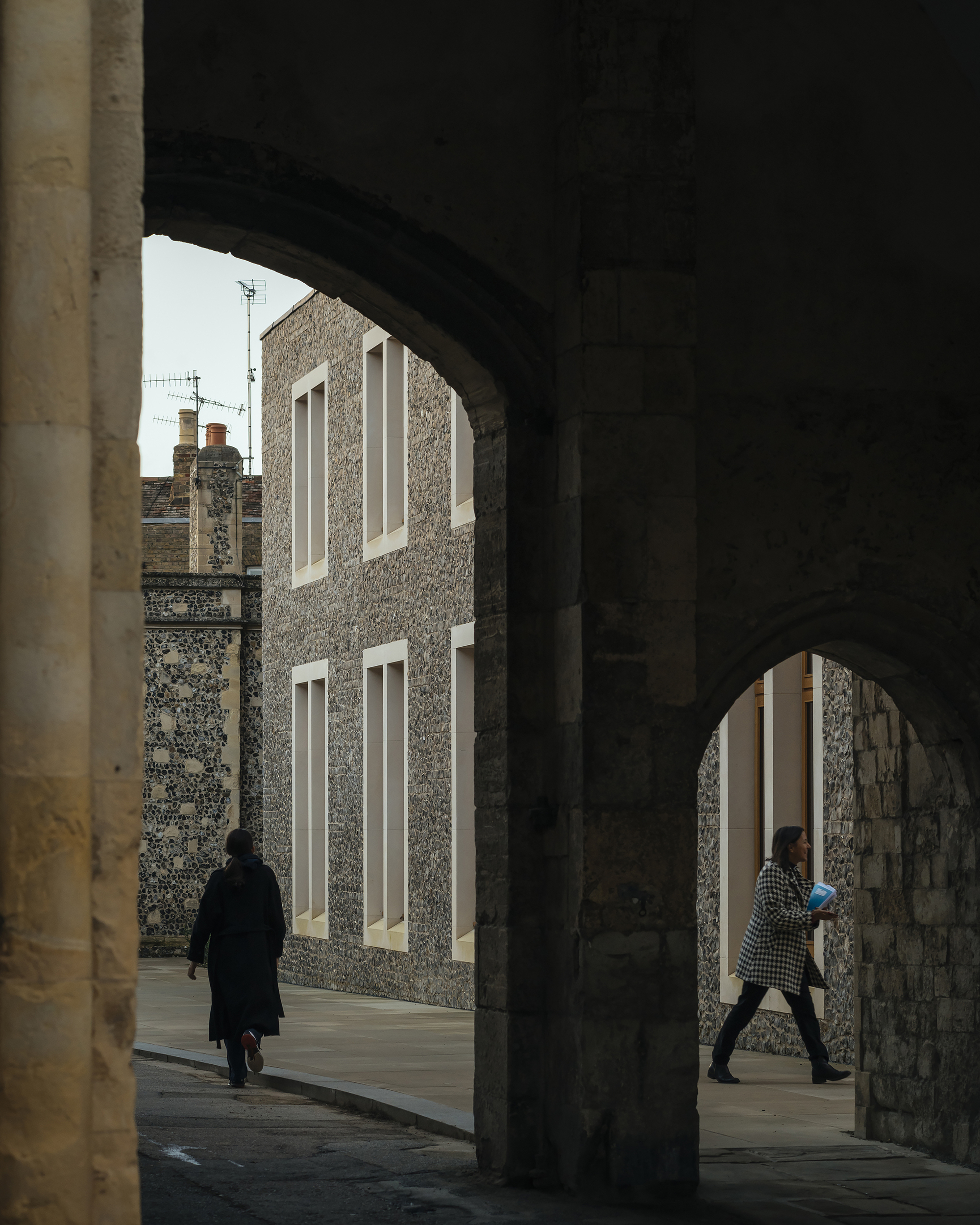 View through a vaulted passage showing the flint facade and two figures walking in opposite directions