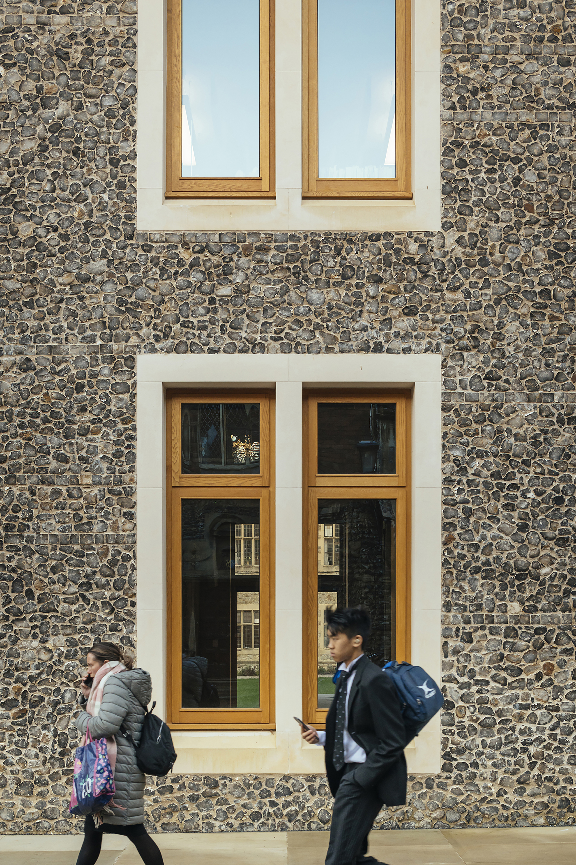 Cobblestone facade with timber-framed windows and two students walking past beneath sunny skies
