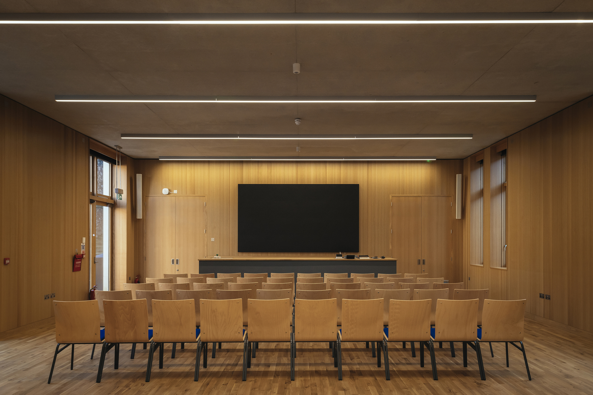 Assembly hall with timber-paneled walls, rows of chairs and recessed linear lighting overhead