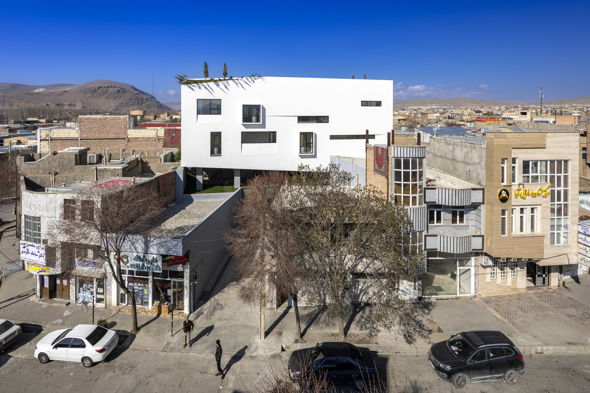 White cubic volume elevated above a dark base with bare winter trees in an arid townscape