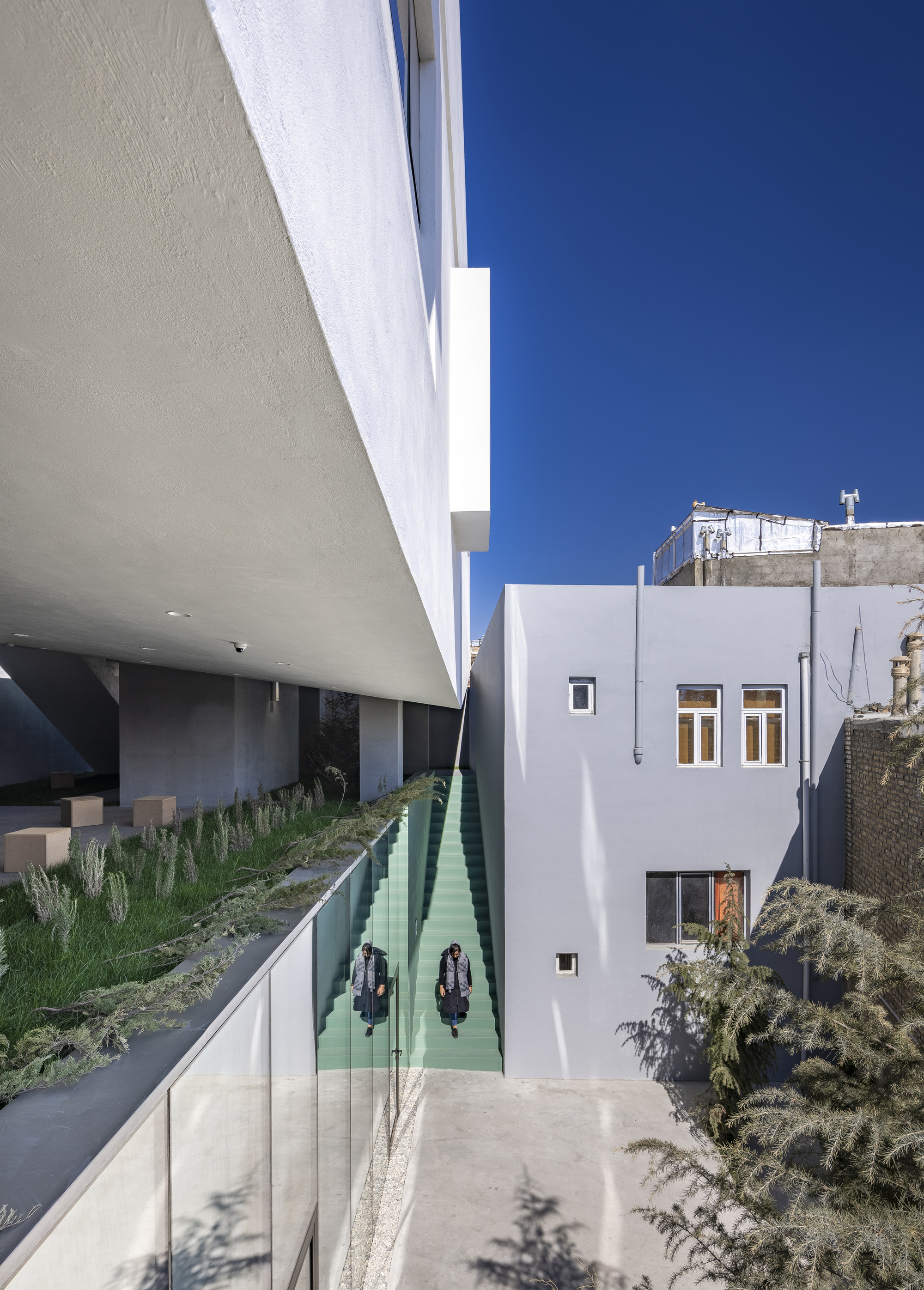 Entry courtyard with mint green reflecting pool beneath a cantilevered white volume in bright sunlight