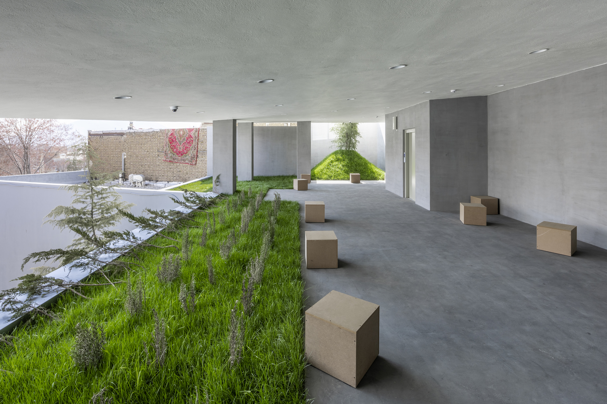 Covered terrace with planted grass strip and cube seating along a polished concrete floor