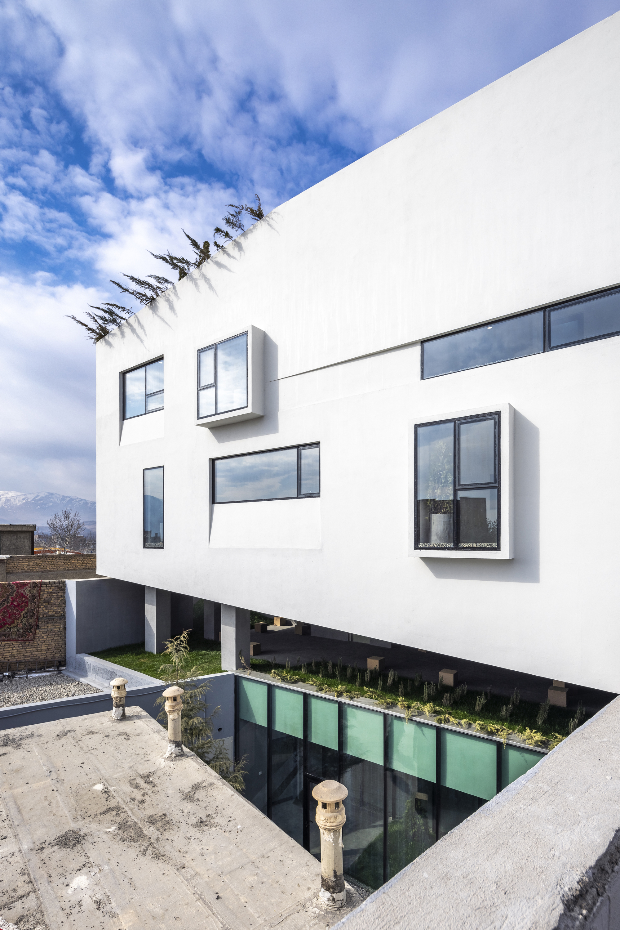 White cantilevered upper floors with protruding bay windows above a sunken courtyard with green glazing