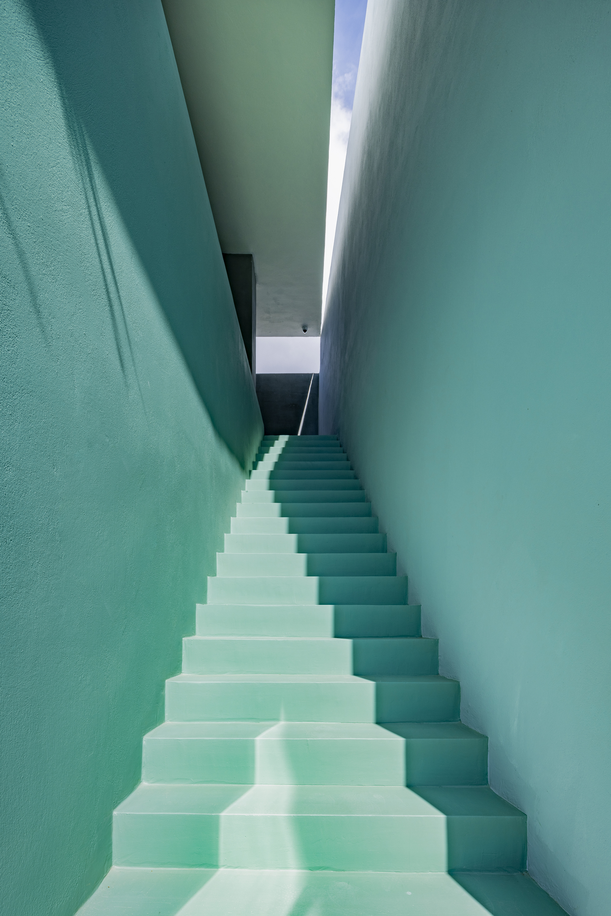 Narrow stairwell with mint green walls and skylight above casting light down the white treads