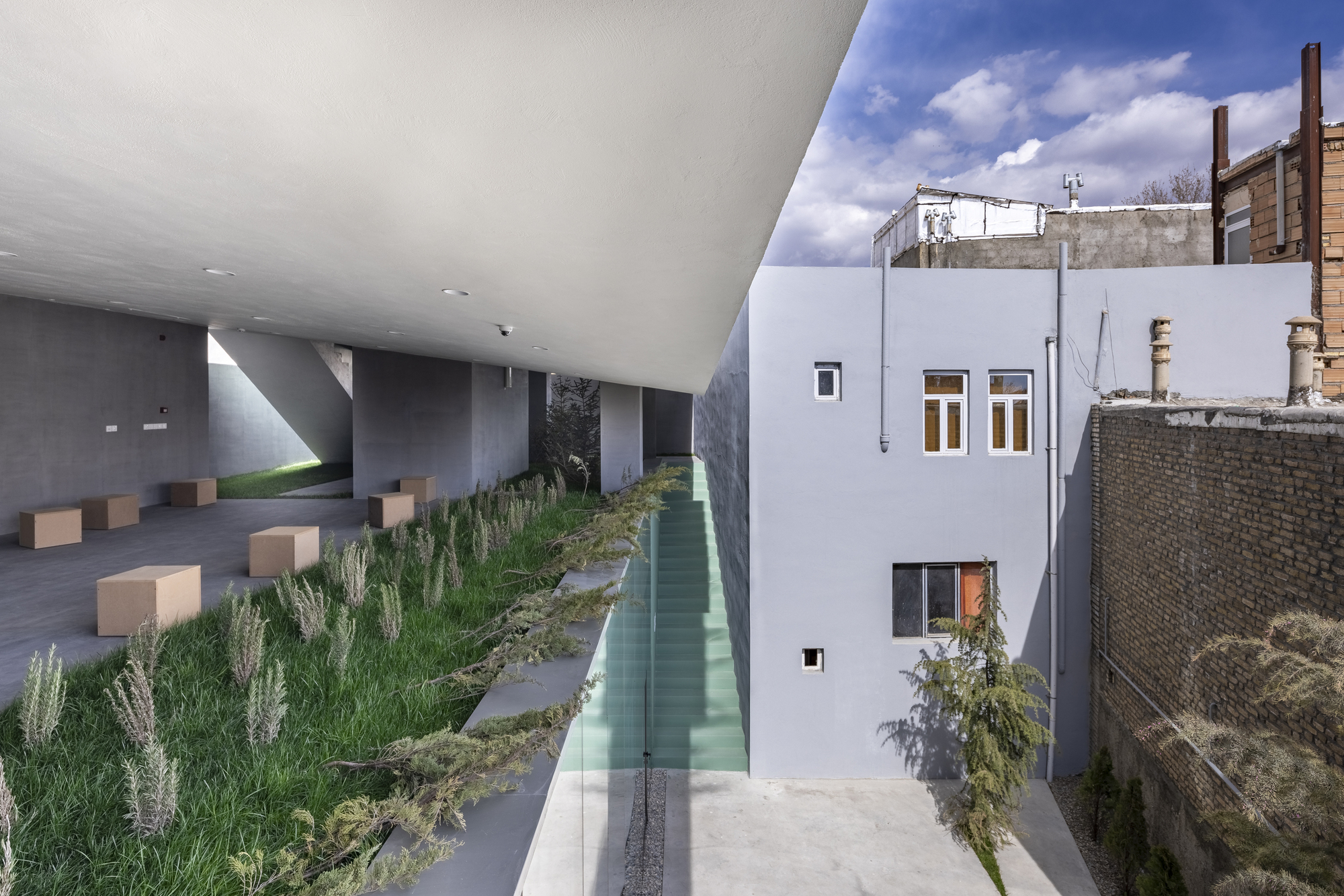 Covered terrace with planted beds and cube seating overlooking courtyard with cloudy sky above