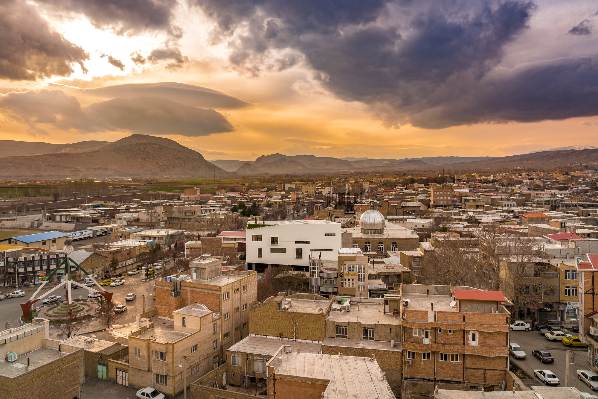White cubic volume emerging from the urban fabric at sunset with mountains in the distance