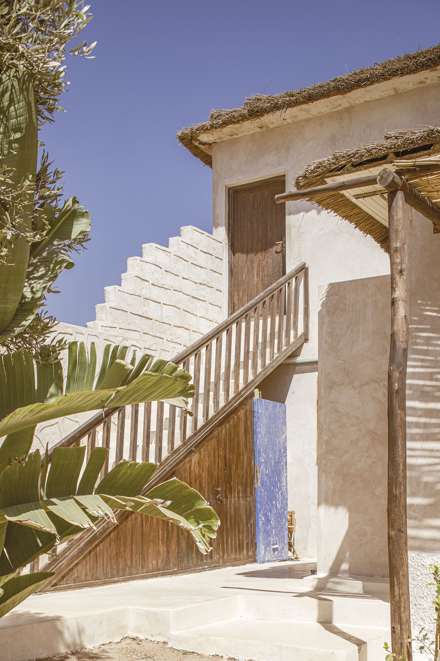 Exterior staircase with slatted timber balustrade connecting courtyard to upper floor door beside banana plants