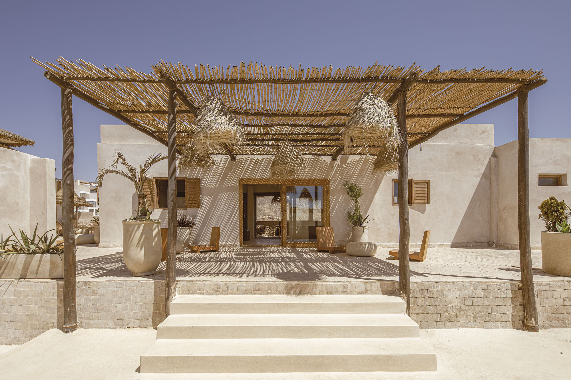 Covered terrace with timber posts, palm frond roof, and thatched pendants suspended over the glazed entrance doors