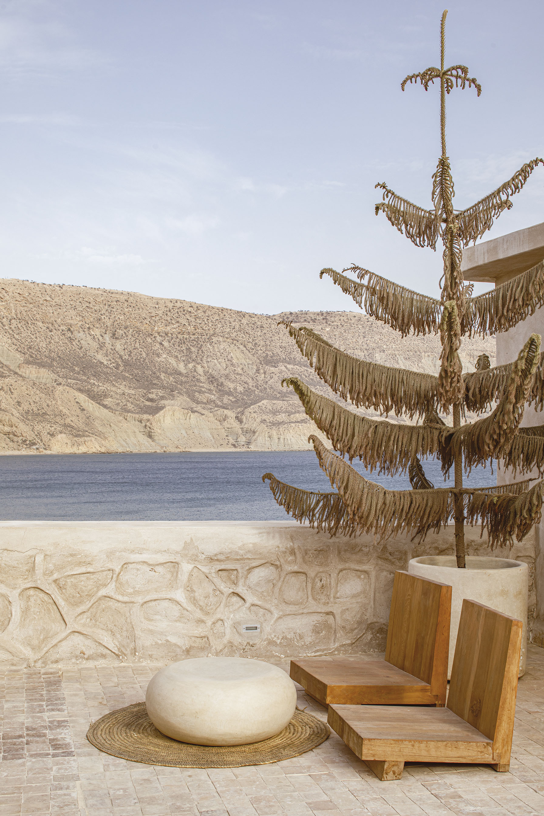 Terrace with decorative rope sculpture on pole beside stone seat wall overlooking water and hills