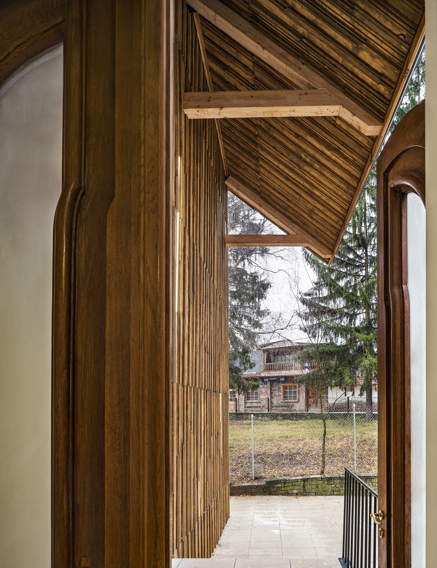 View through timber-lined arched doorway toward an exterior courtyard with bare winter trees