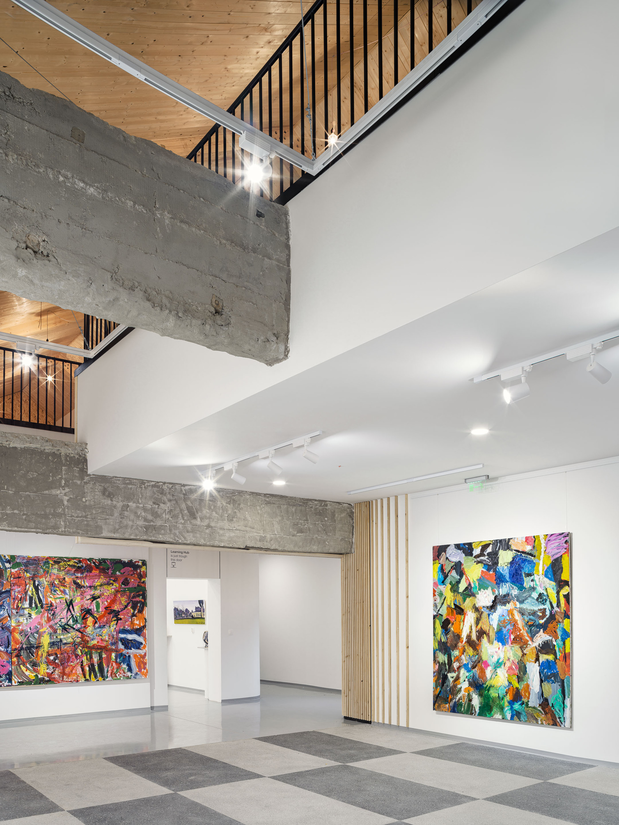 Double-height gallery space with exposed concrete beams and timber slat screens between floor levels