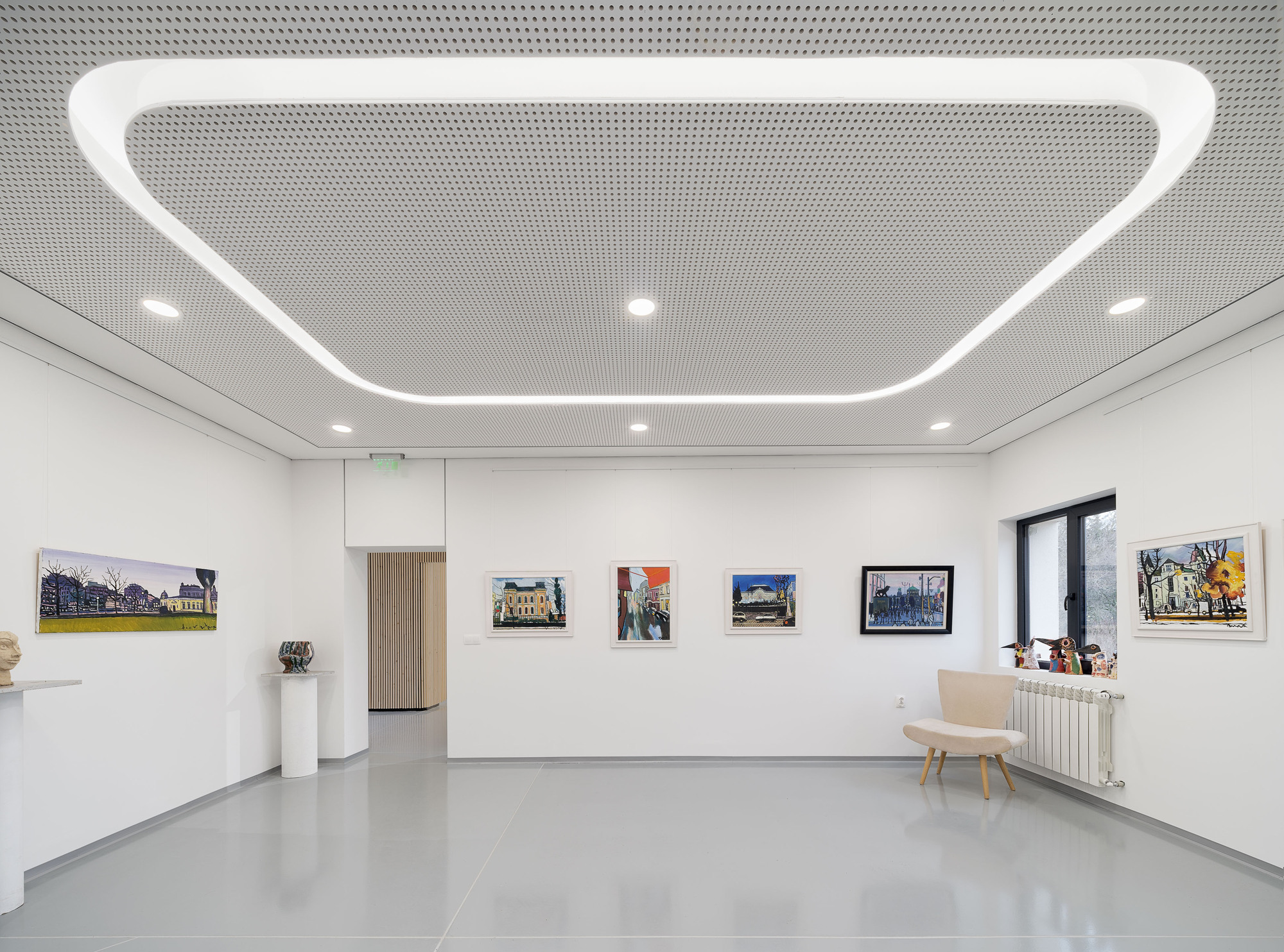Gallery space with white walls displaying framed artworks and a curved linear ceiling light