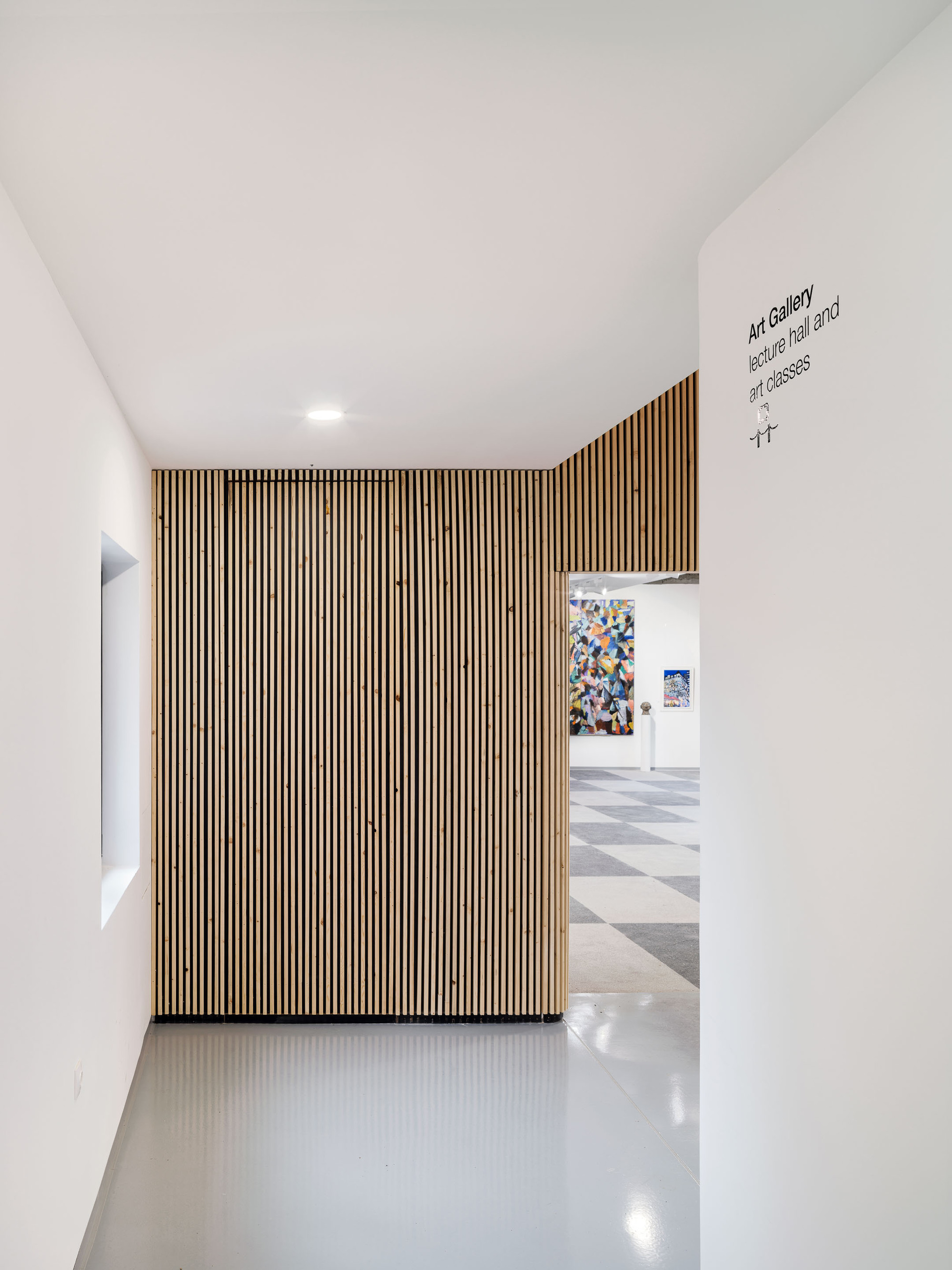 White corridor with vertical timber slat wall leading to gallery space beyond