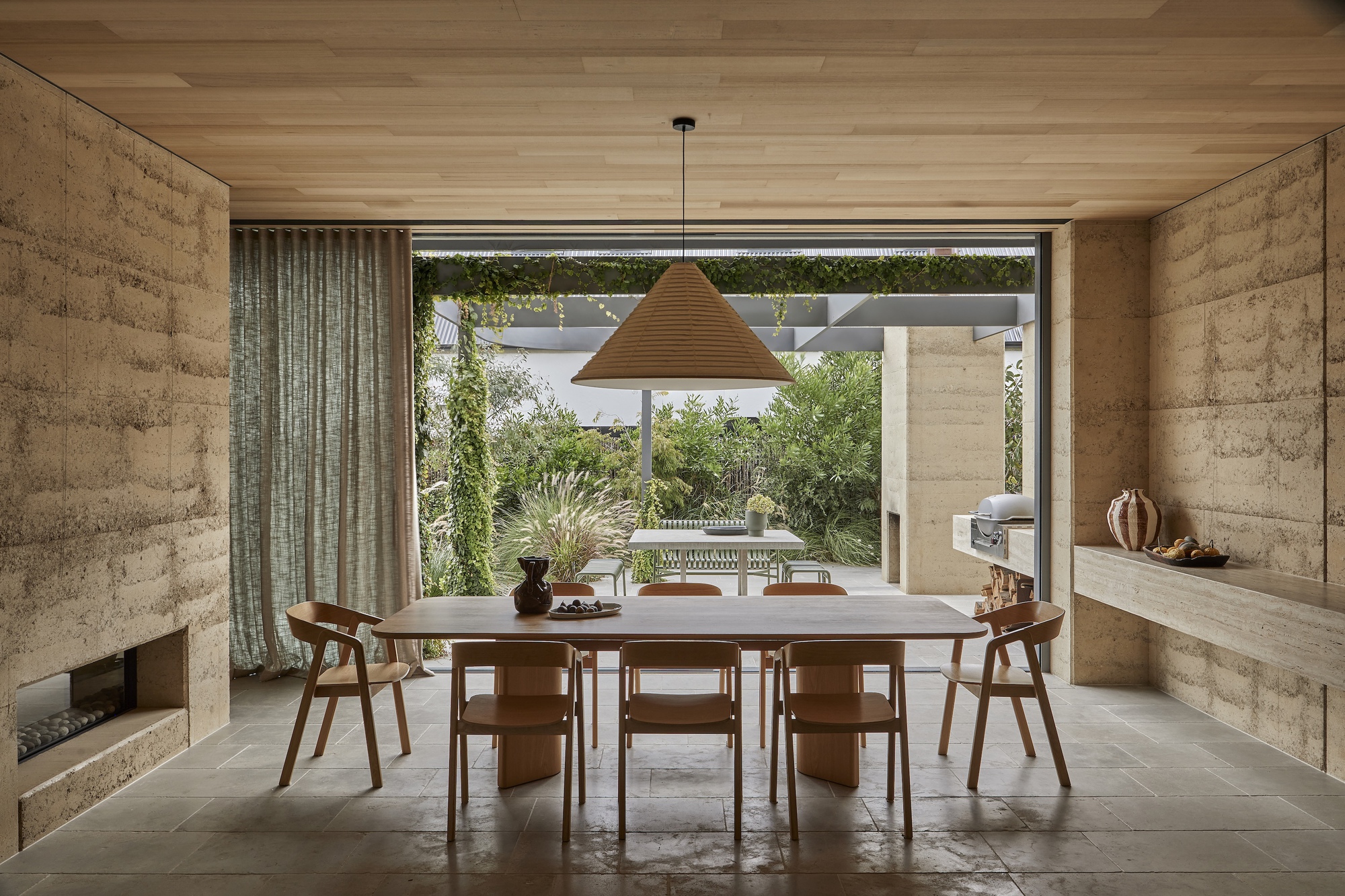 Dining room with rammed earth walls and timber ceiling opening to a planted courtyard
