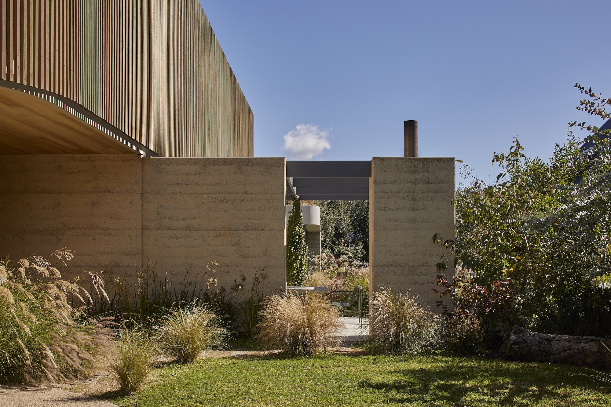 Rammed earth walls framing a courtyard with ornamental grasses under clear sky
