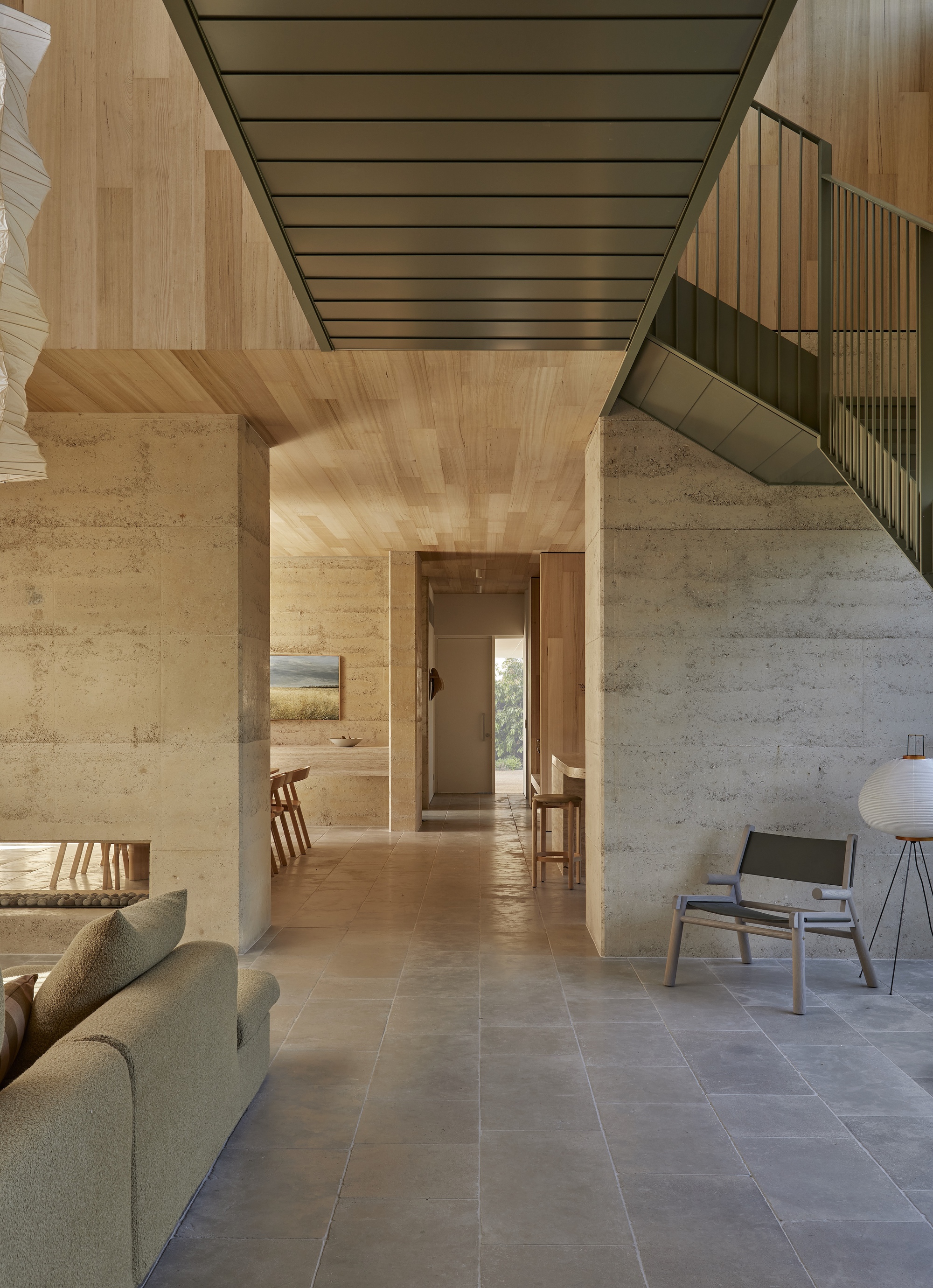 Interior corridor with rammed earth column, timber ceiling and view through to distant doorway