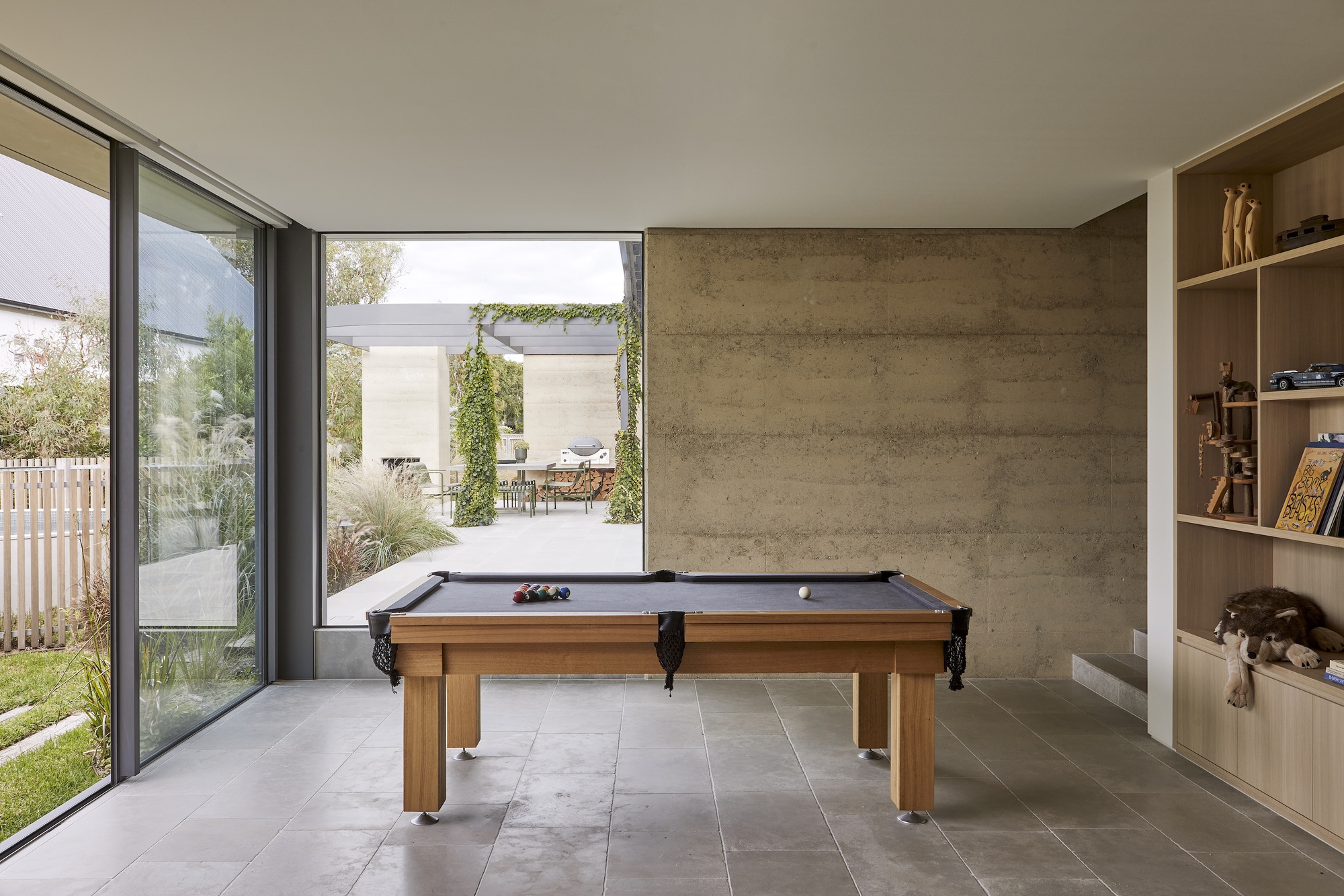 Games room with billiards table looking through sliding glass doors to planted courtyard beyond