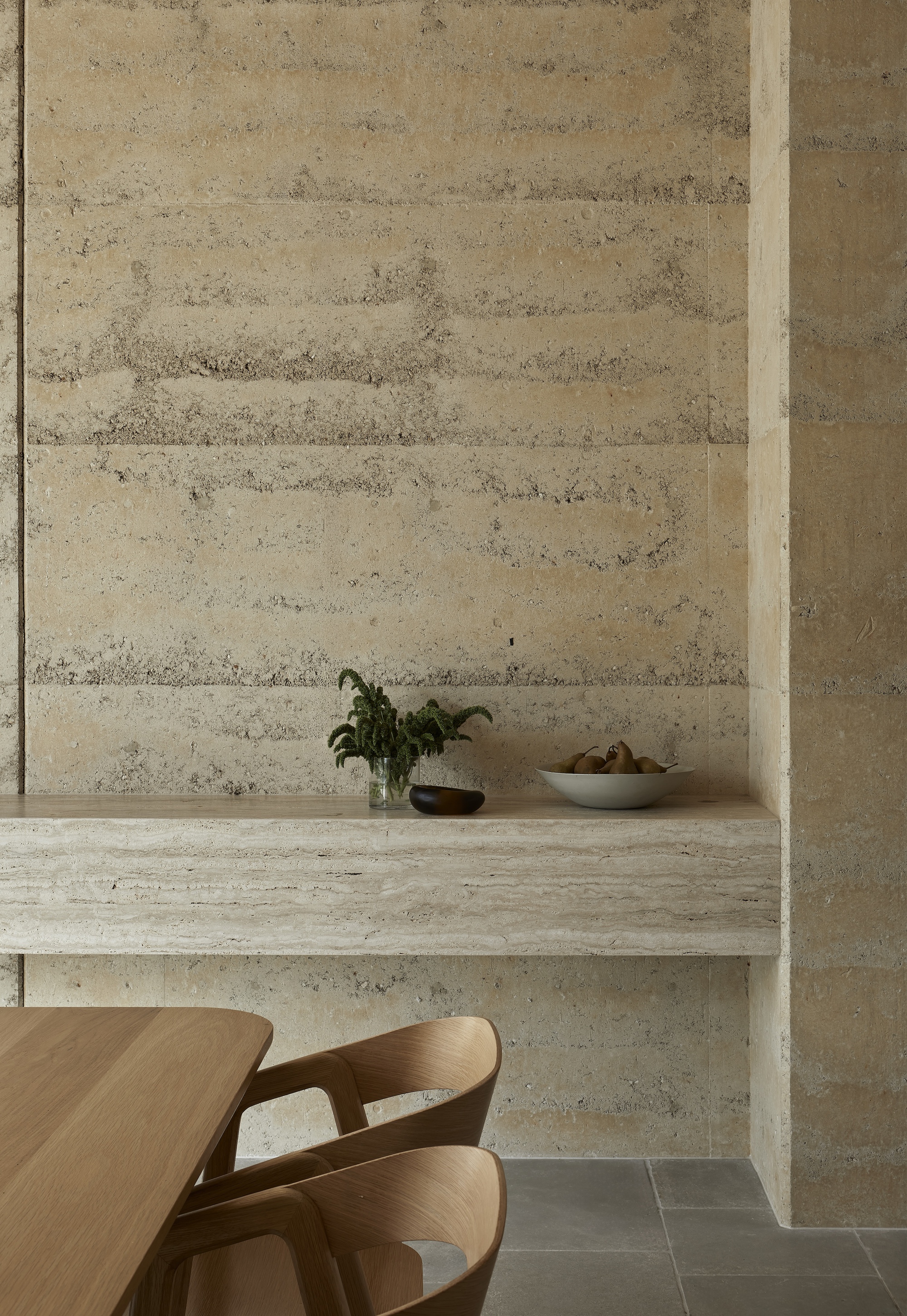Built-in rammed earth bench with potted plant and fruit bowl against horizontal grain wall