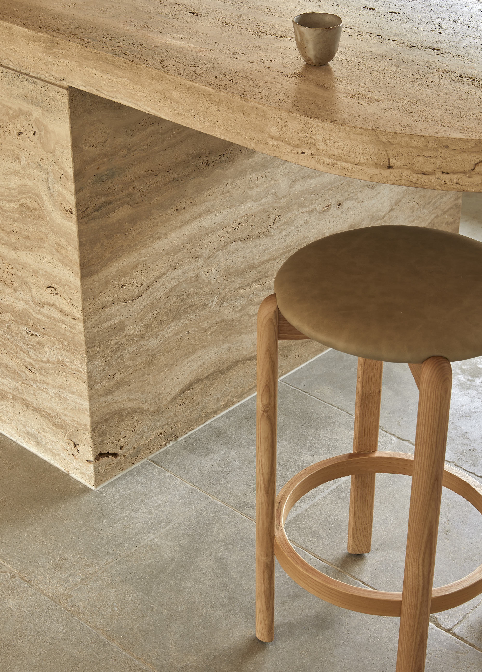 Close-up of travertine island bench meeting a timber stool with exposed leg joinery