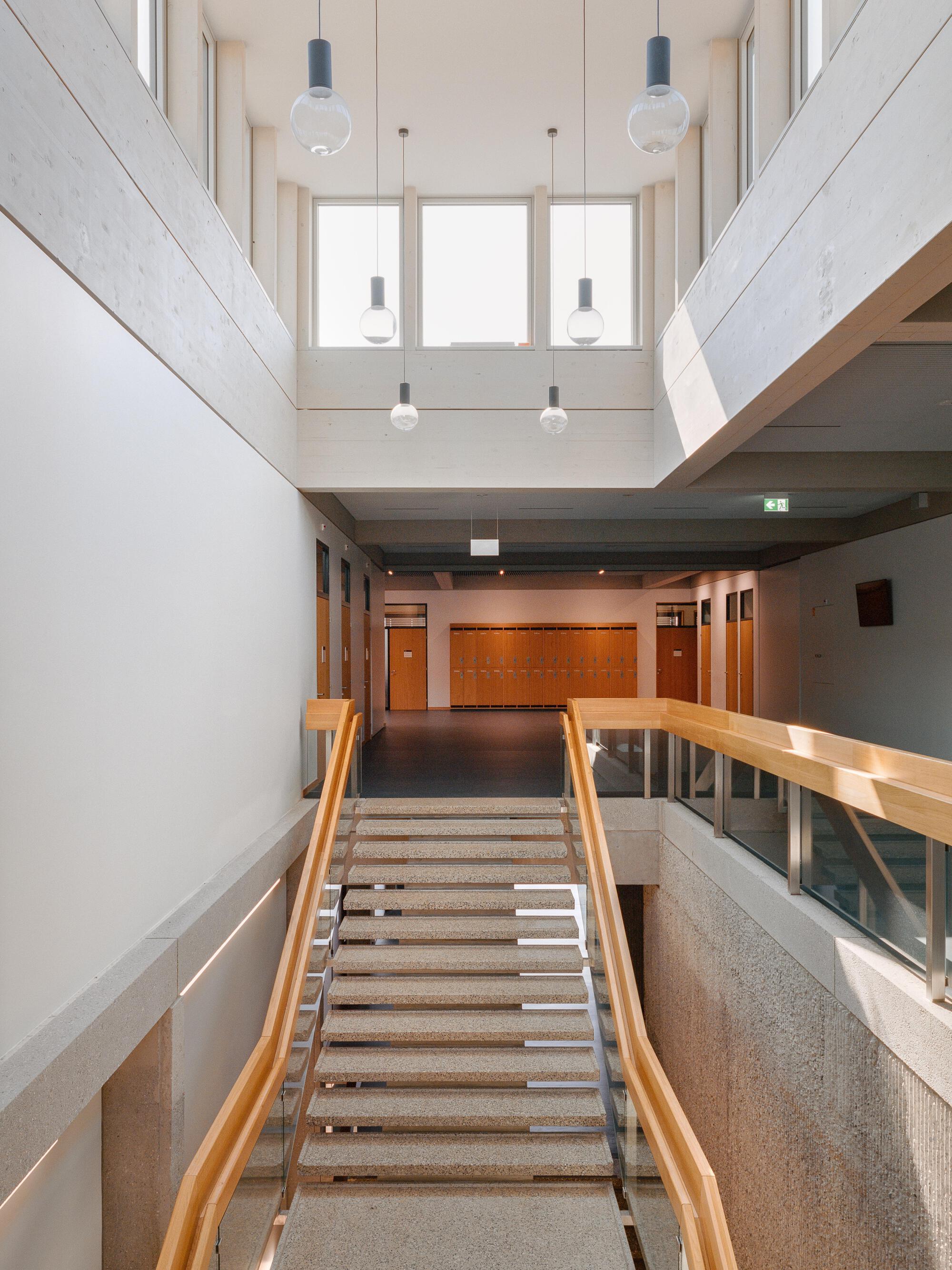 Interior atrium with terrazzo stairs, timber handrails, and pendant lights below a skylight