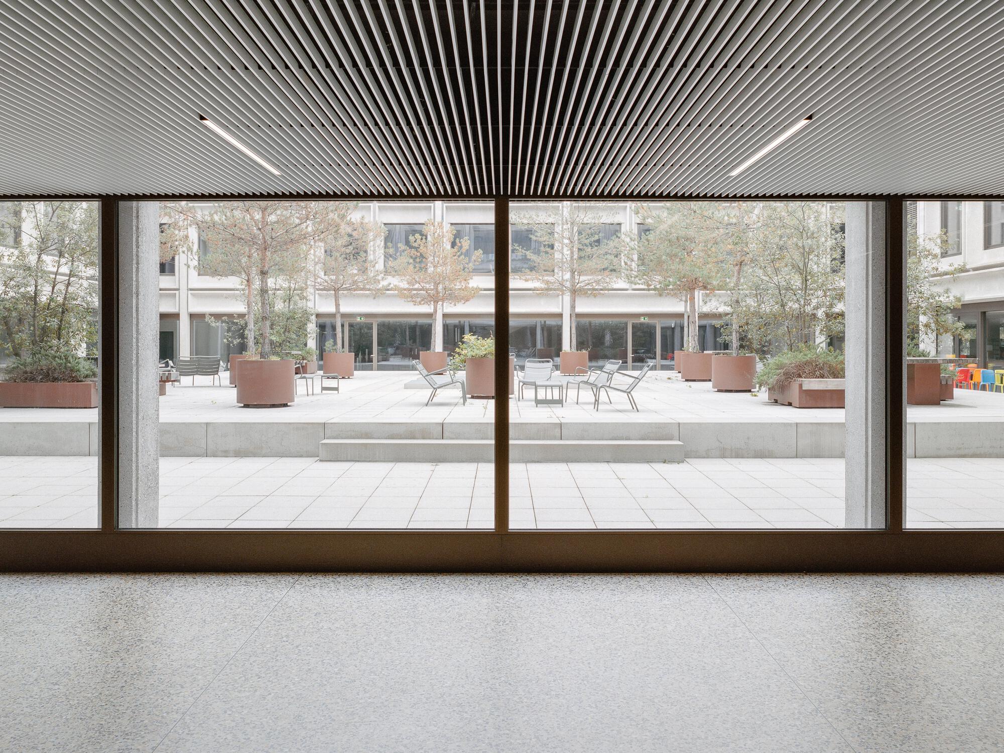 Interior view through bronze-framed glazing overlooking the courtyard with slatted wood ceiling overhead