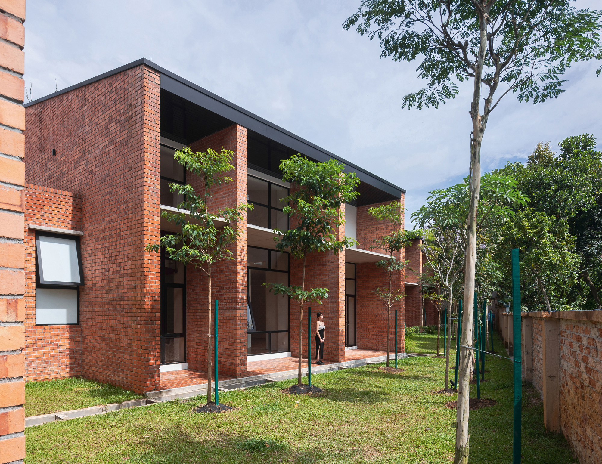 Rear facade with tall glazed openings framed by brick piers in a garden with young trees