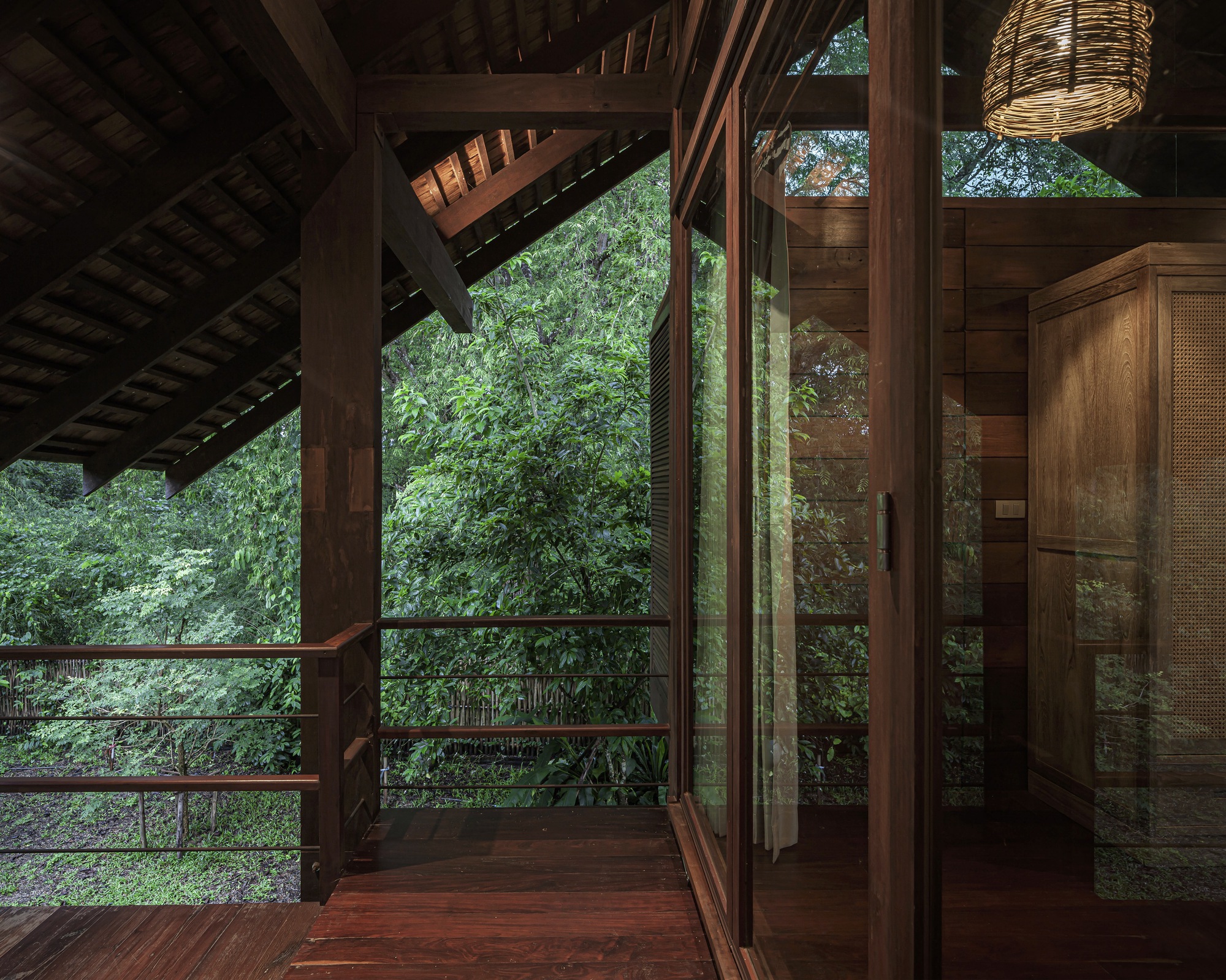Covered timber terrace opening to garden foliage through floor-to-ceiling glazing with exposed rafters above