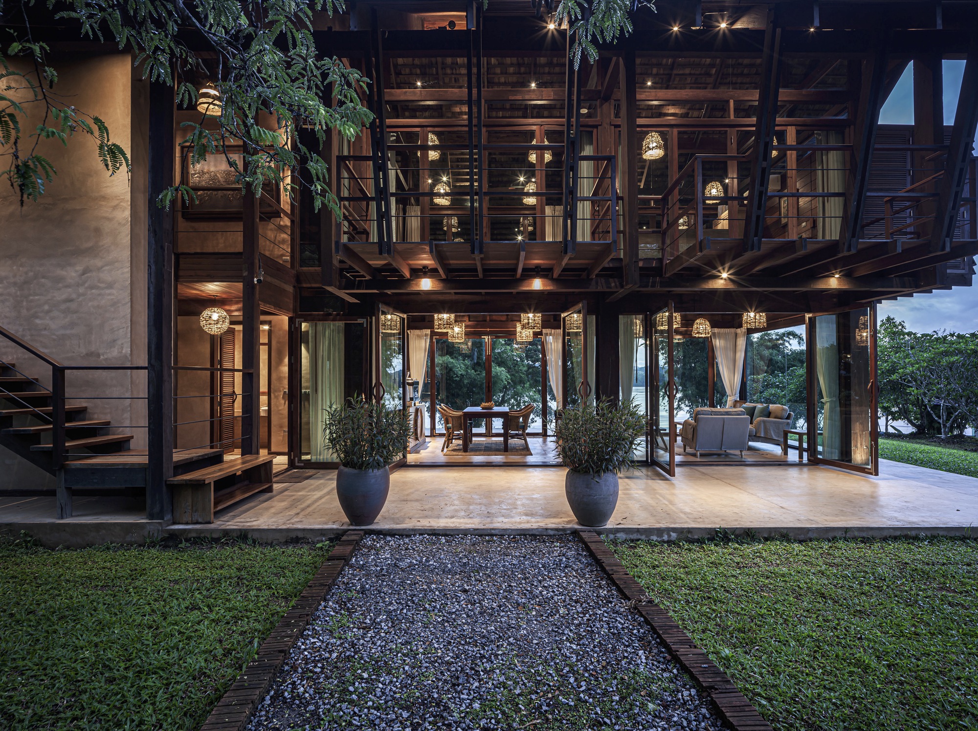 Evening view of raised timber pavilion on columns with pendant lighting and planters at entry