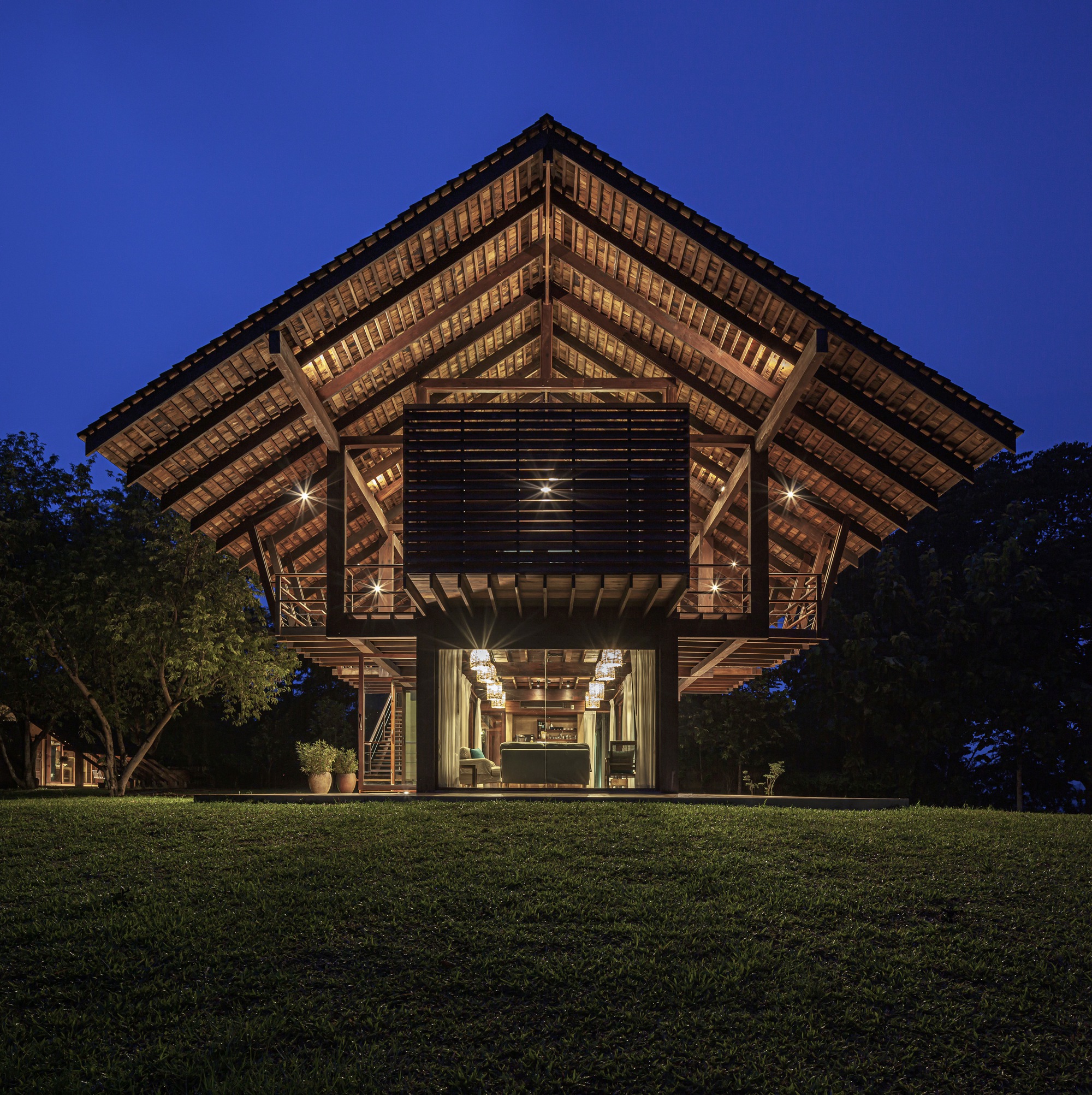 Front elevation showing the timber-framed pavilion with exposed rafters and louvered screen at dusk