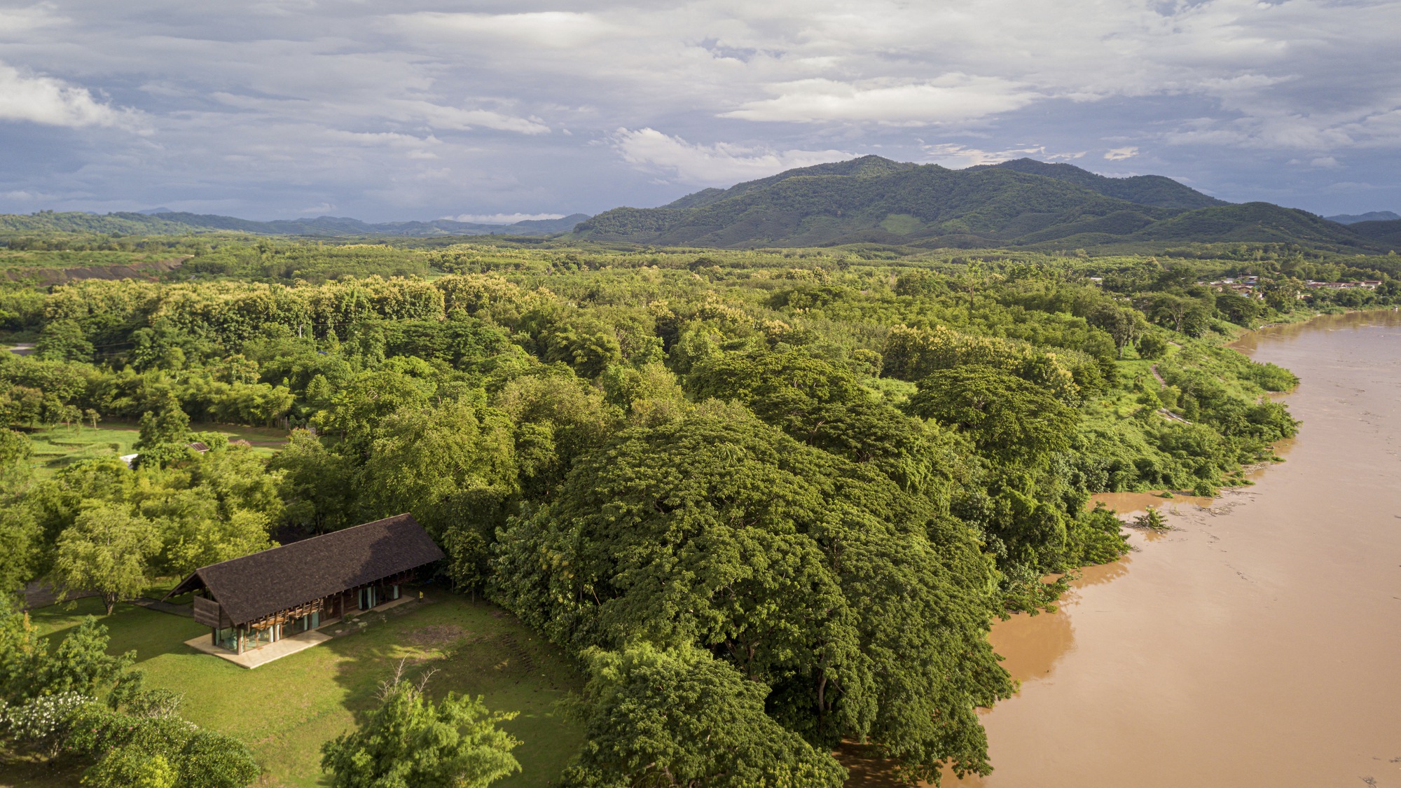 Aerial view of the low-pitched roof structure nestled among dense tree canopy beside a muddy river