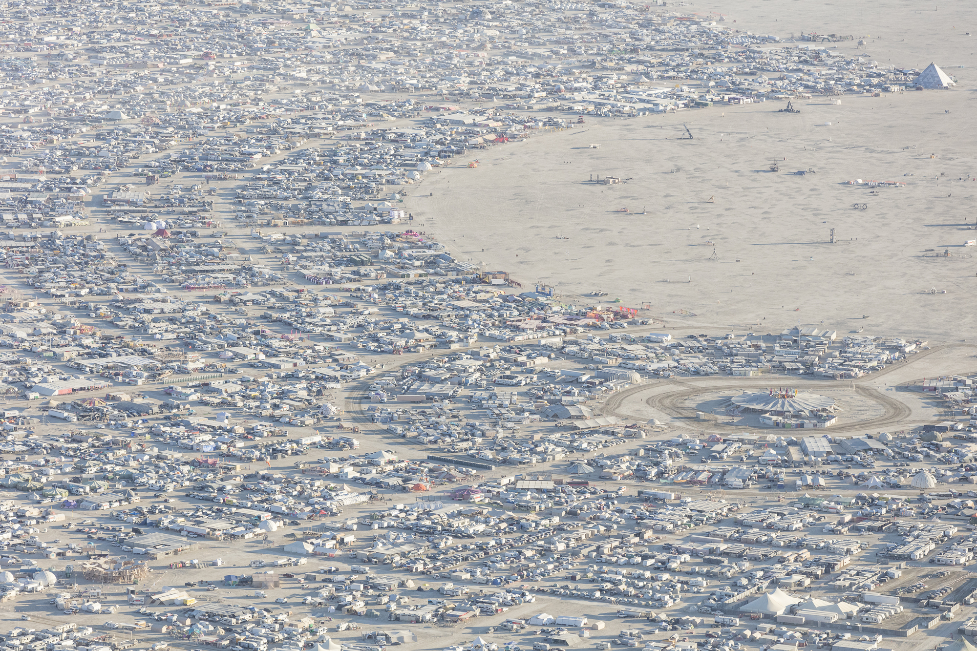 Aerial view of temporary encampment scattered across desert with curving pathways and central installations