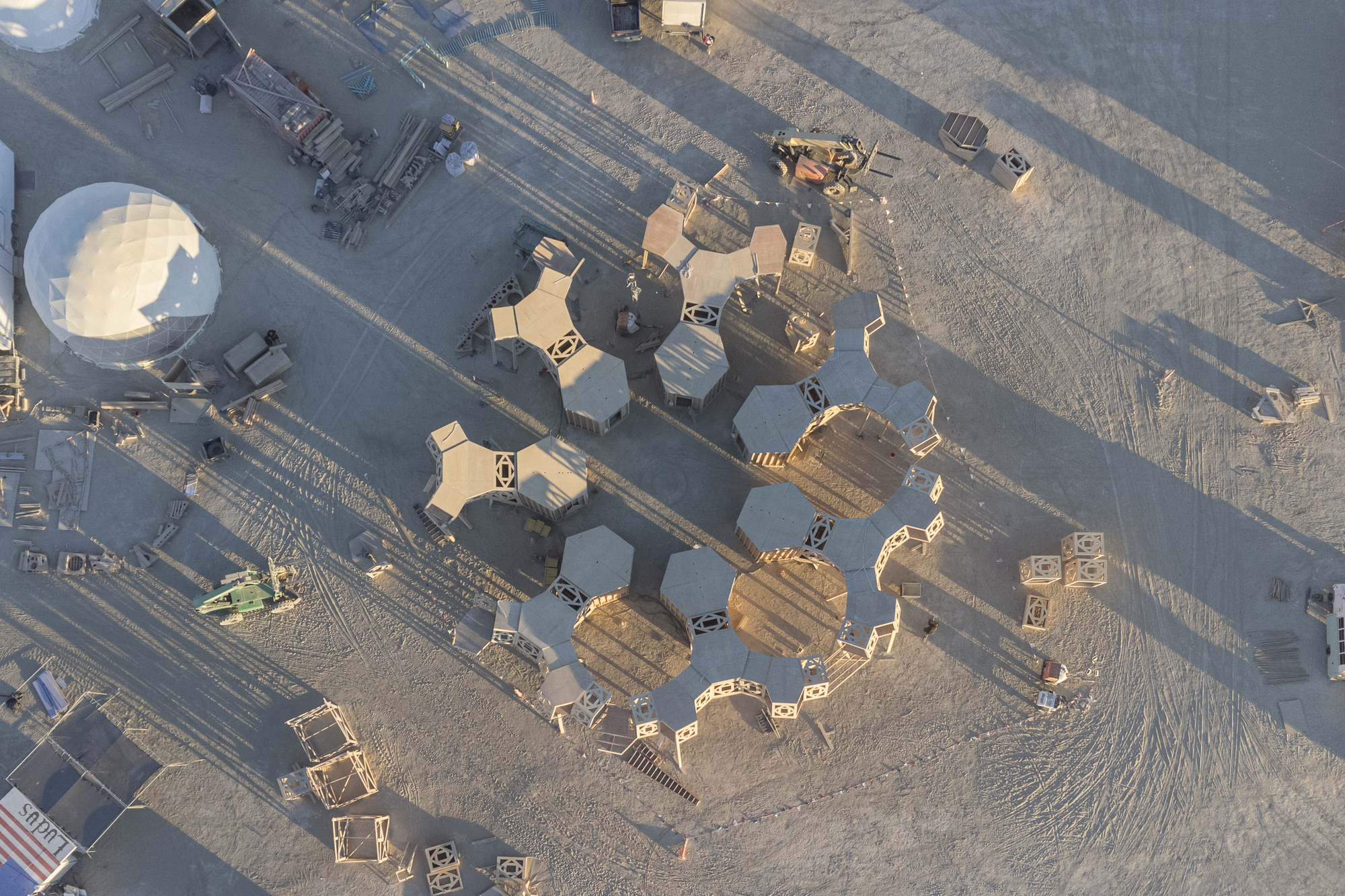 Drone view of hexagonal timber modules clustered on desert playa beside roadway at dawn