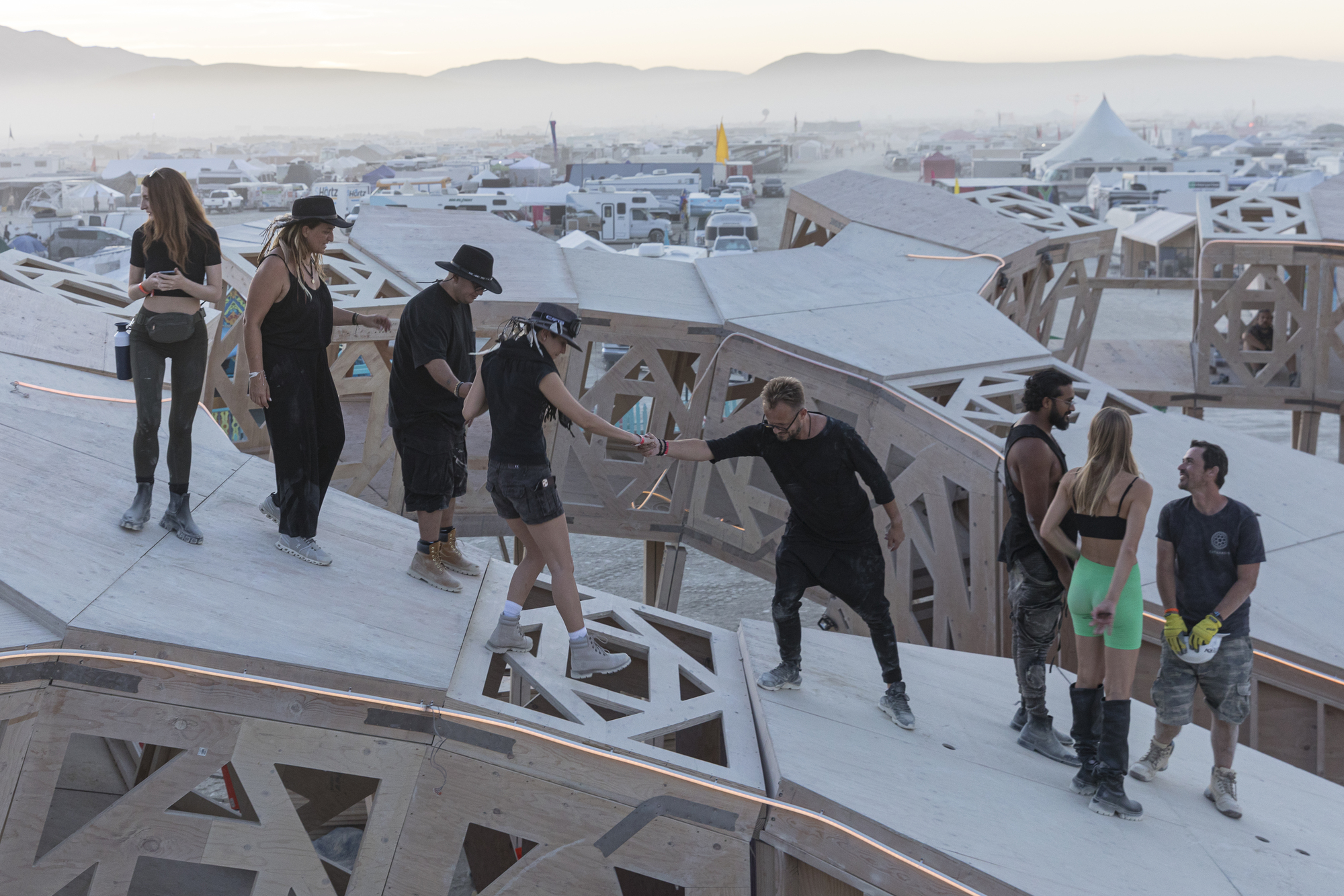 Rooftop deck with angled timber trusses and visitors gathered at dusk overlooking distant mountains