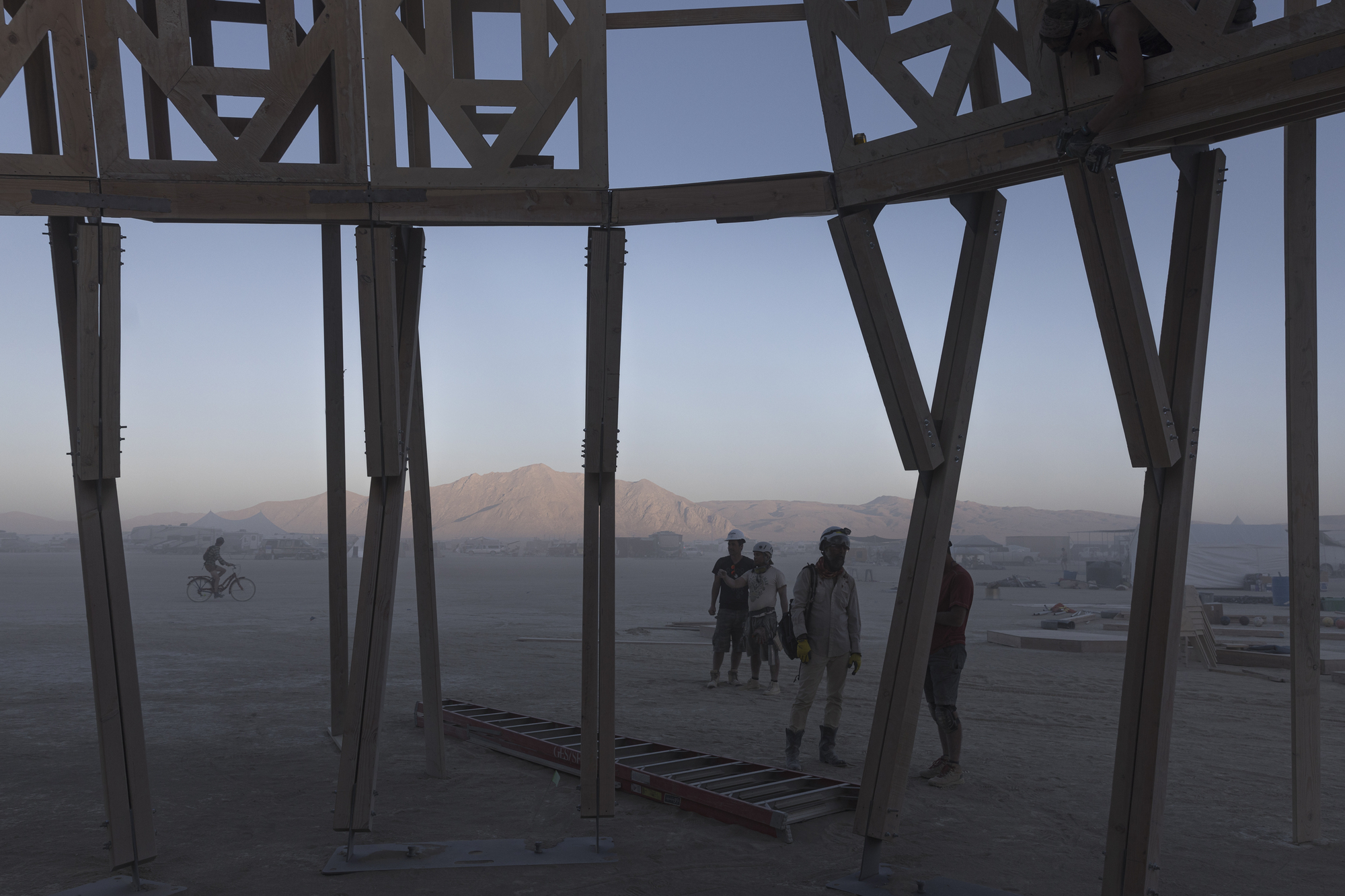 Interior view through angled timber columns framing visitors and distant mountains at twilight