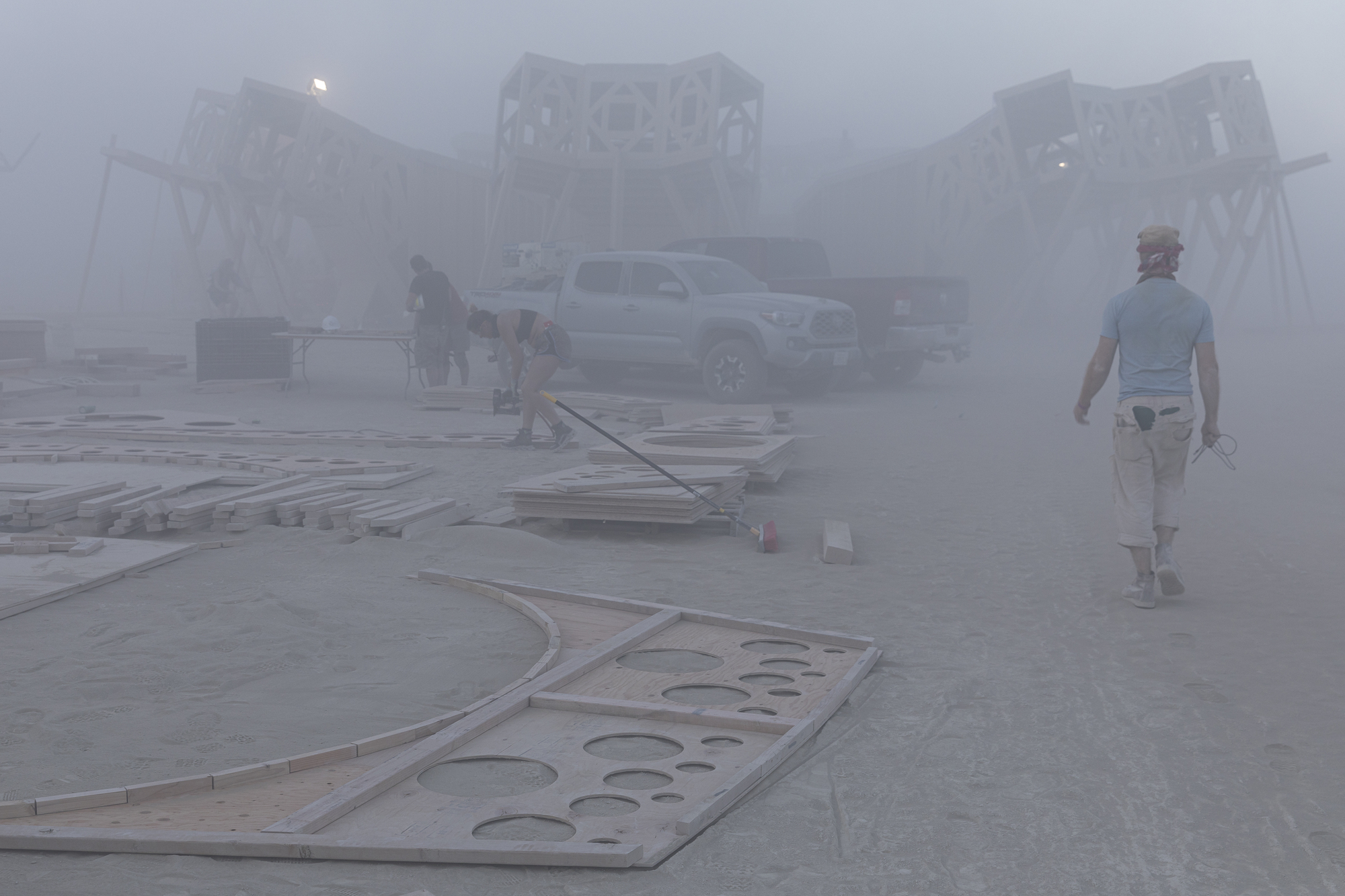 Curved perforated plywood roof panels laid out on the ground during construction in heavy fog