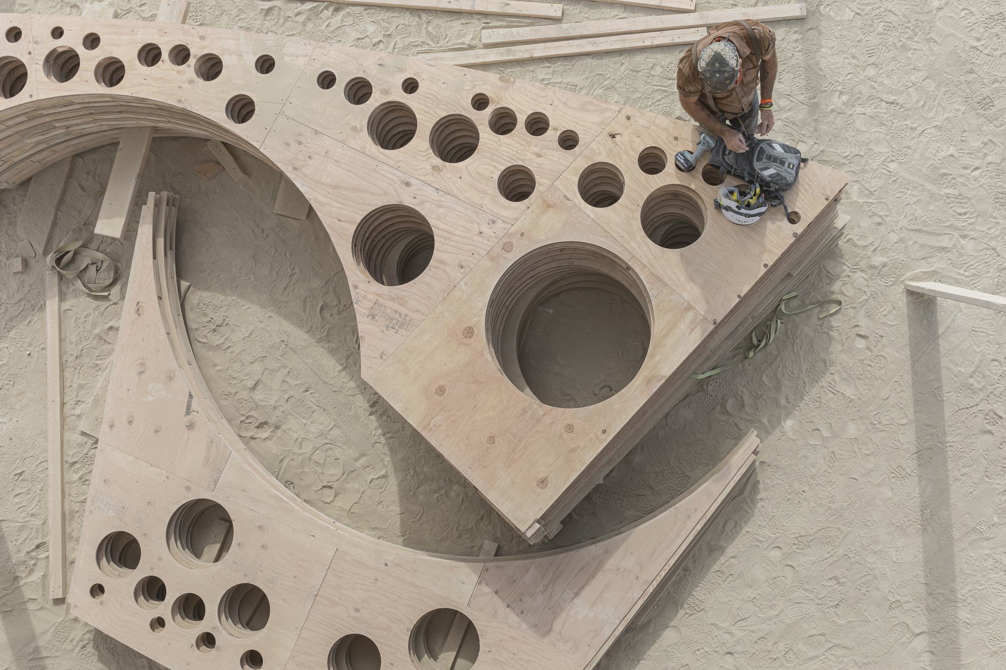 Overhead view of curved plywood panels with circular perforations as a worker applies finish
