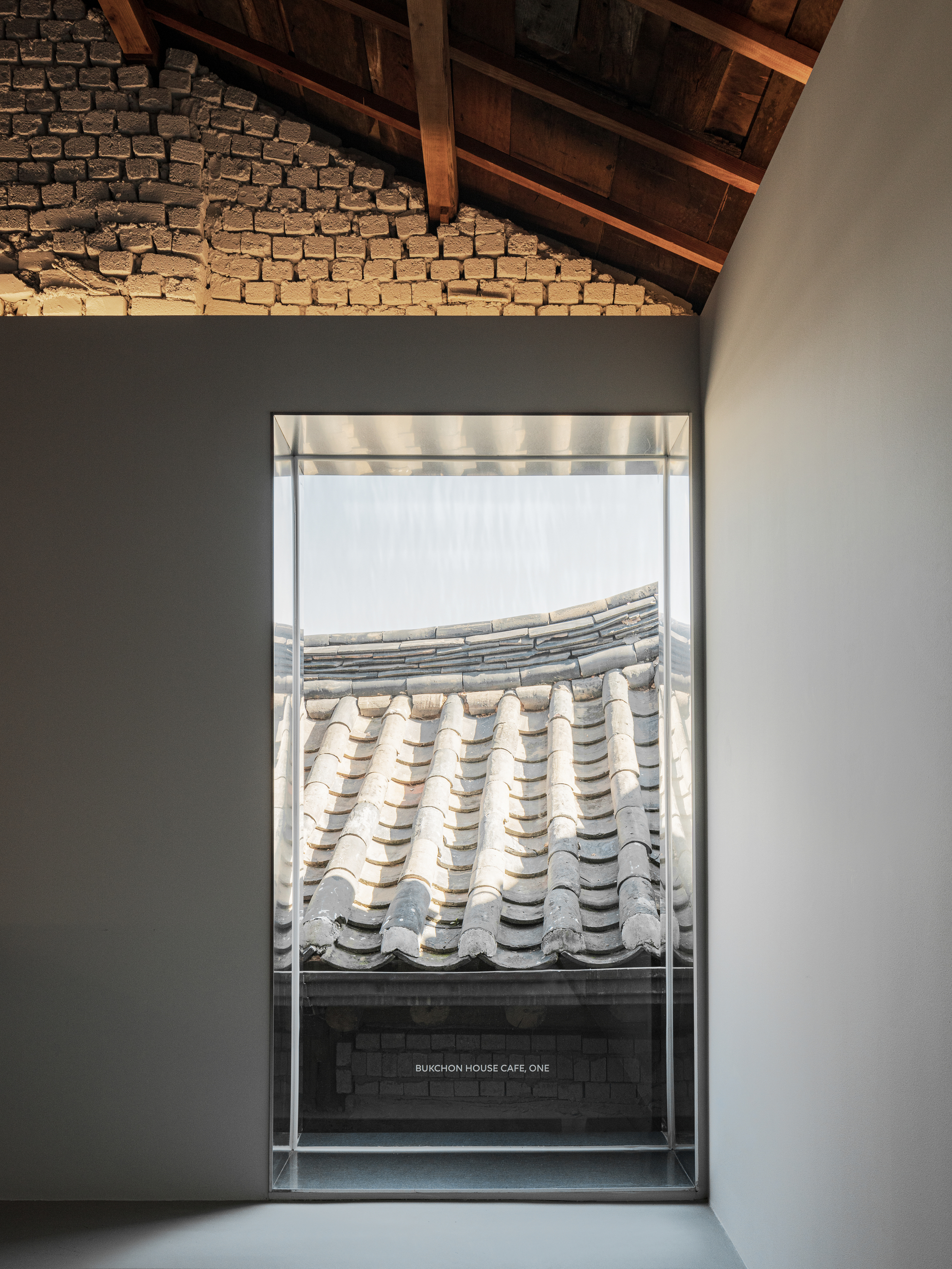 Framed window view of curved ceramic roof tiles beneath exposed timber rafters and grey brick