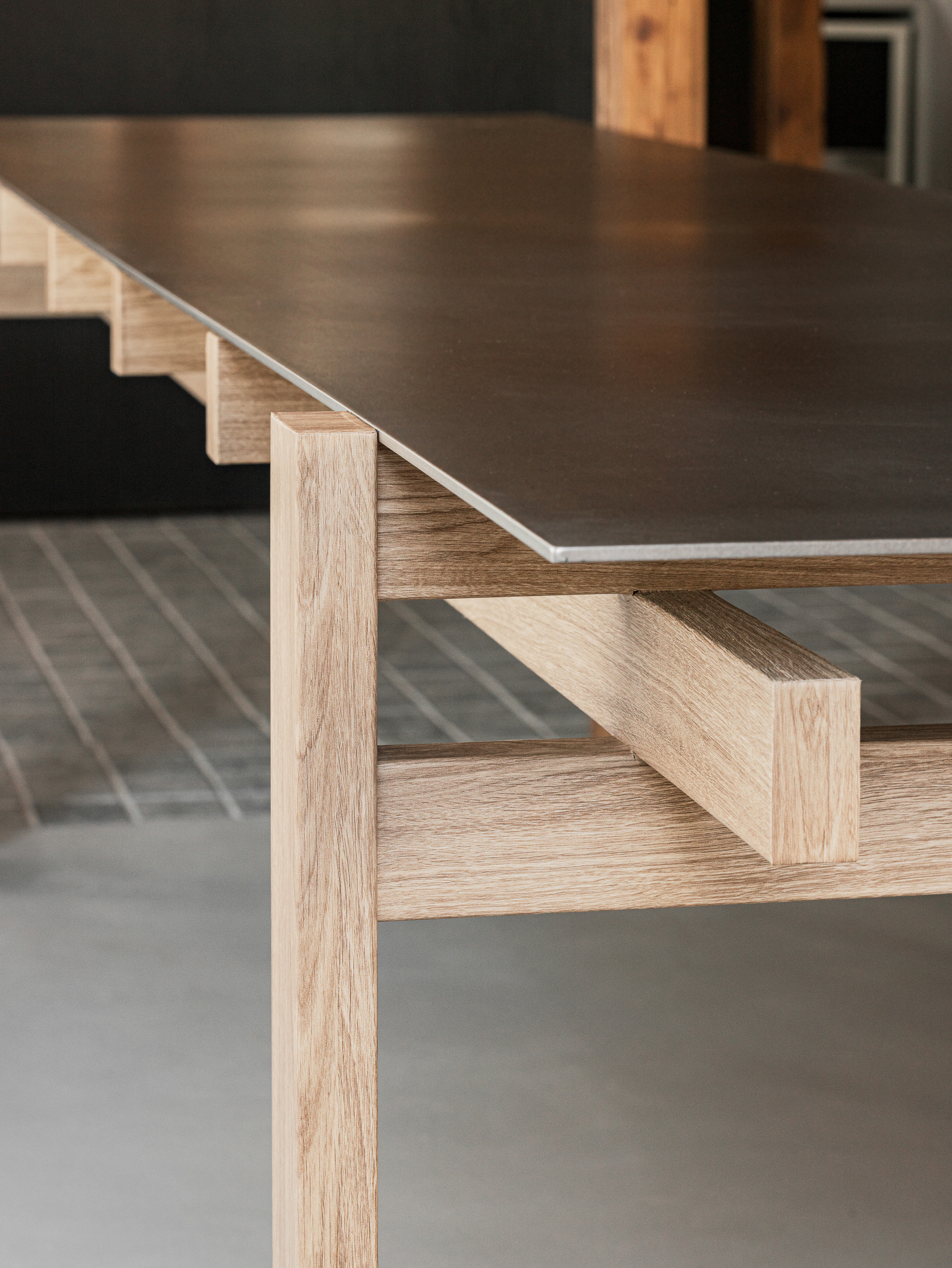 Close-up of a table with light oak frame and dark metal top on polished concrete flooring