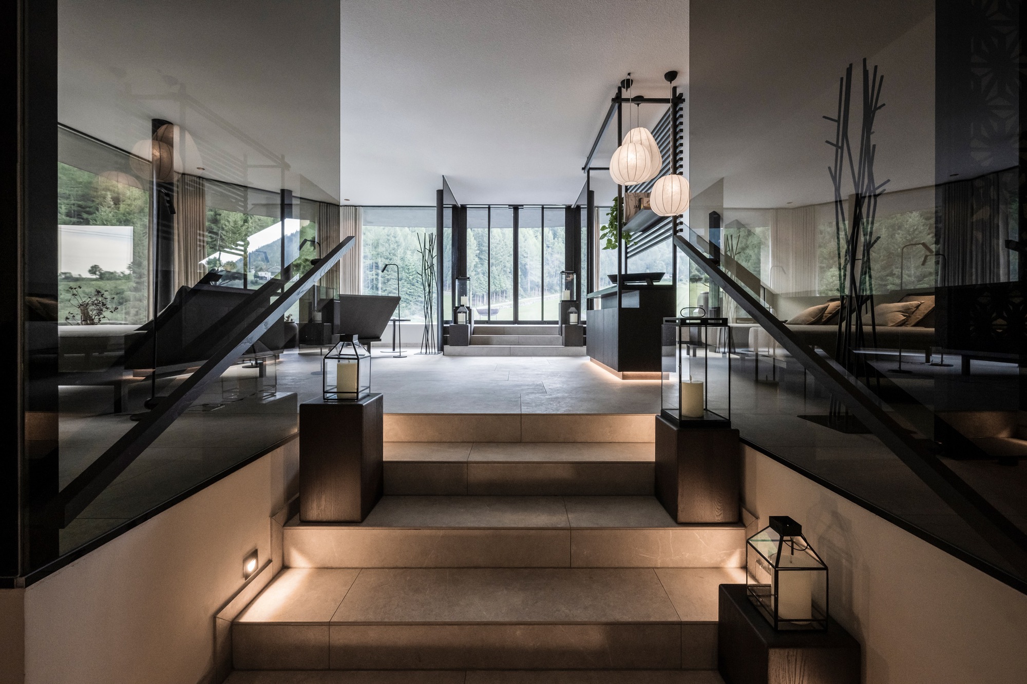 Illuminated stone staircase with glass railings ascending toward glazed entrance vestibule in evening light
