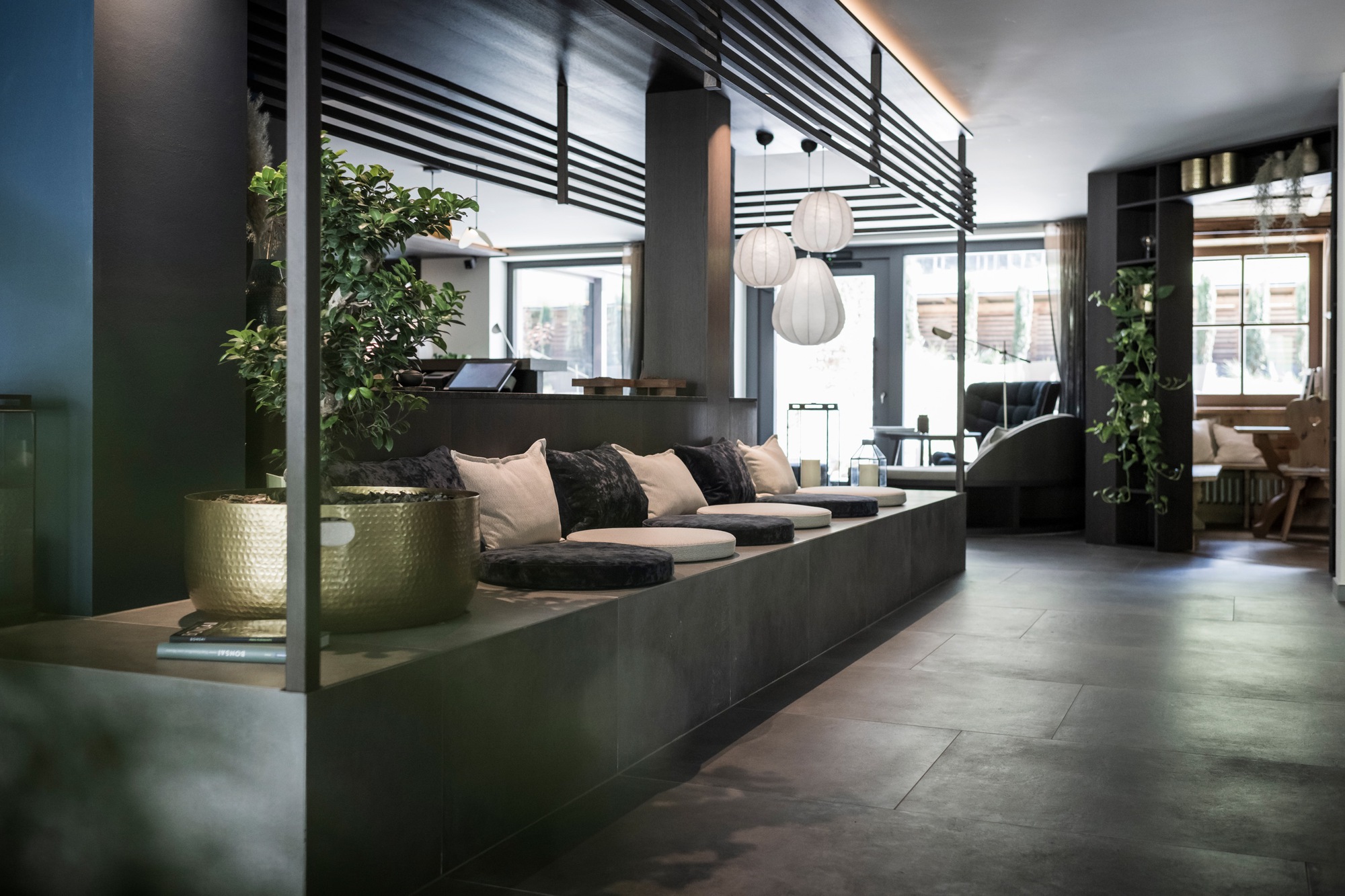 Lounge area with concrete seating platform, horizontal metal screen and brass planters under overcast daylight