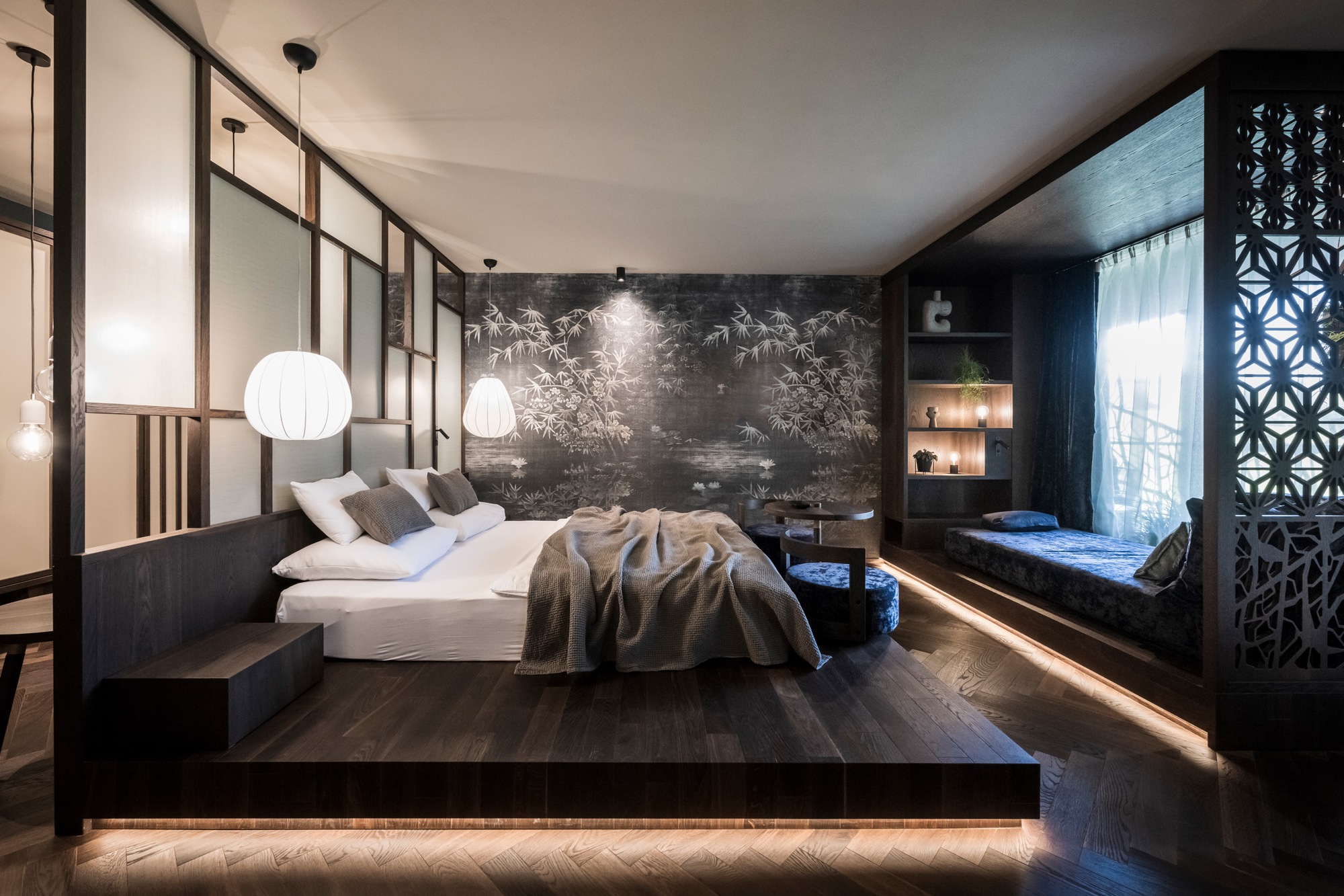 Platform bed with underlit perimeter set against dark botanical wallpaper under pendant globe fixtures