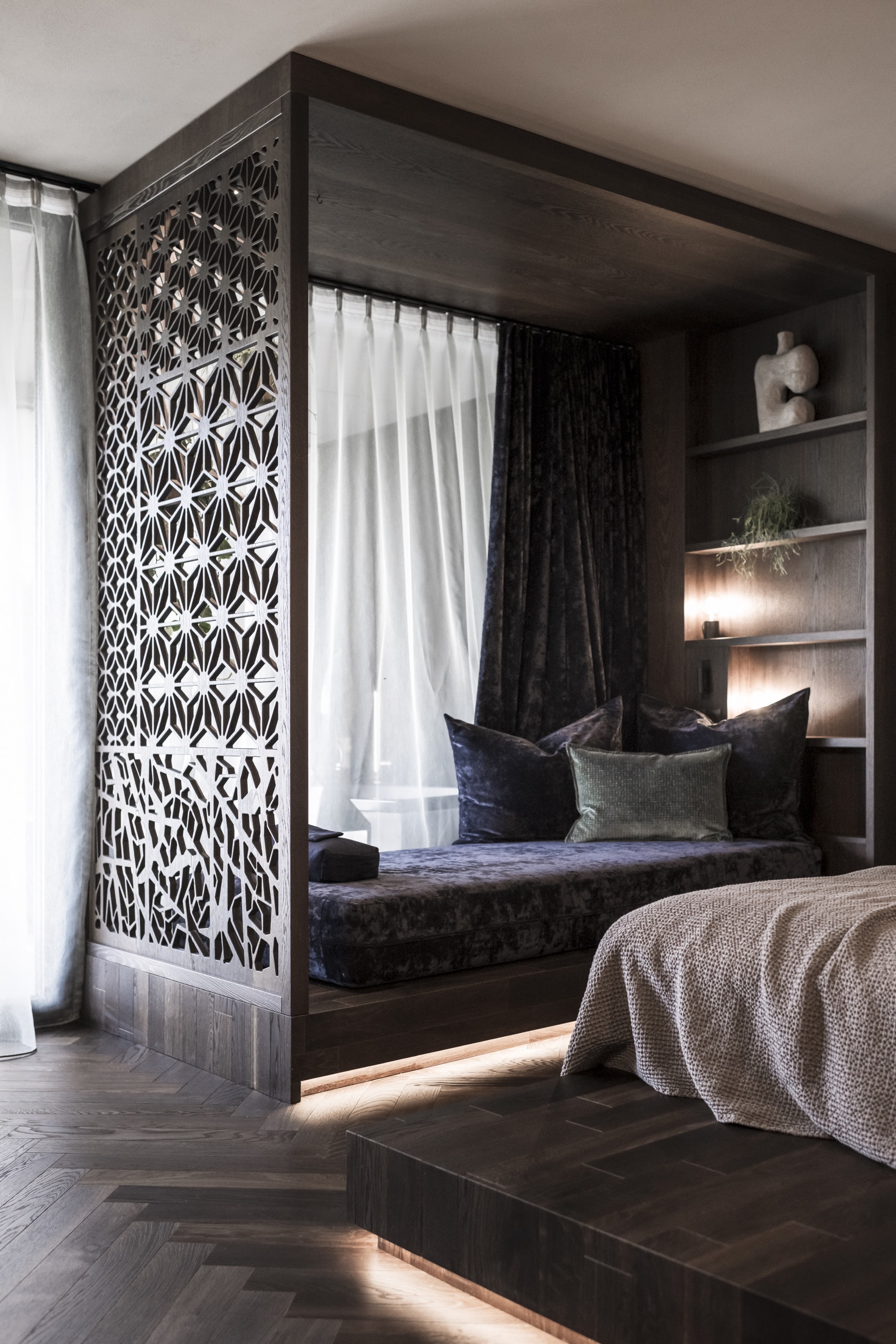 Geometric lattice screen wrapping the corner of a built-in window seat niche with shelving