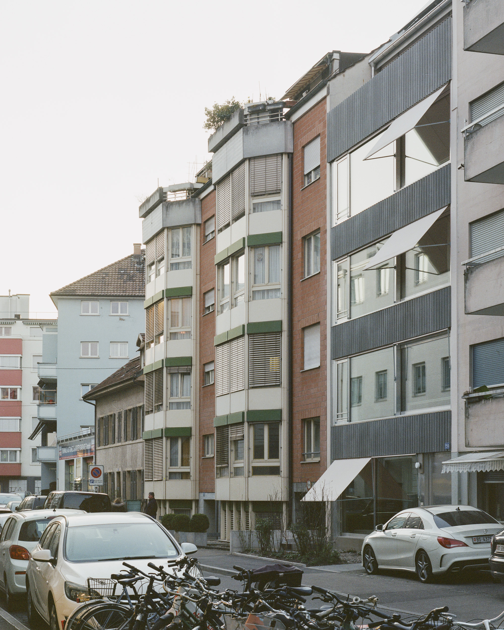 Streetscape showing a mix of residential buildings with metal cladding, brick and balconies with parked cars and bicycles