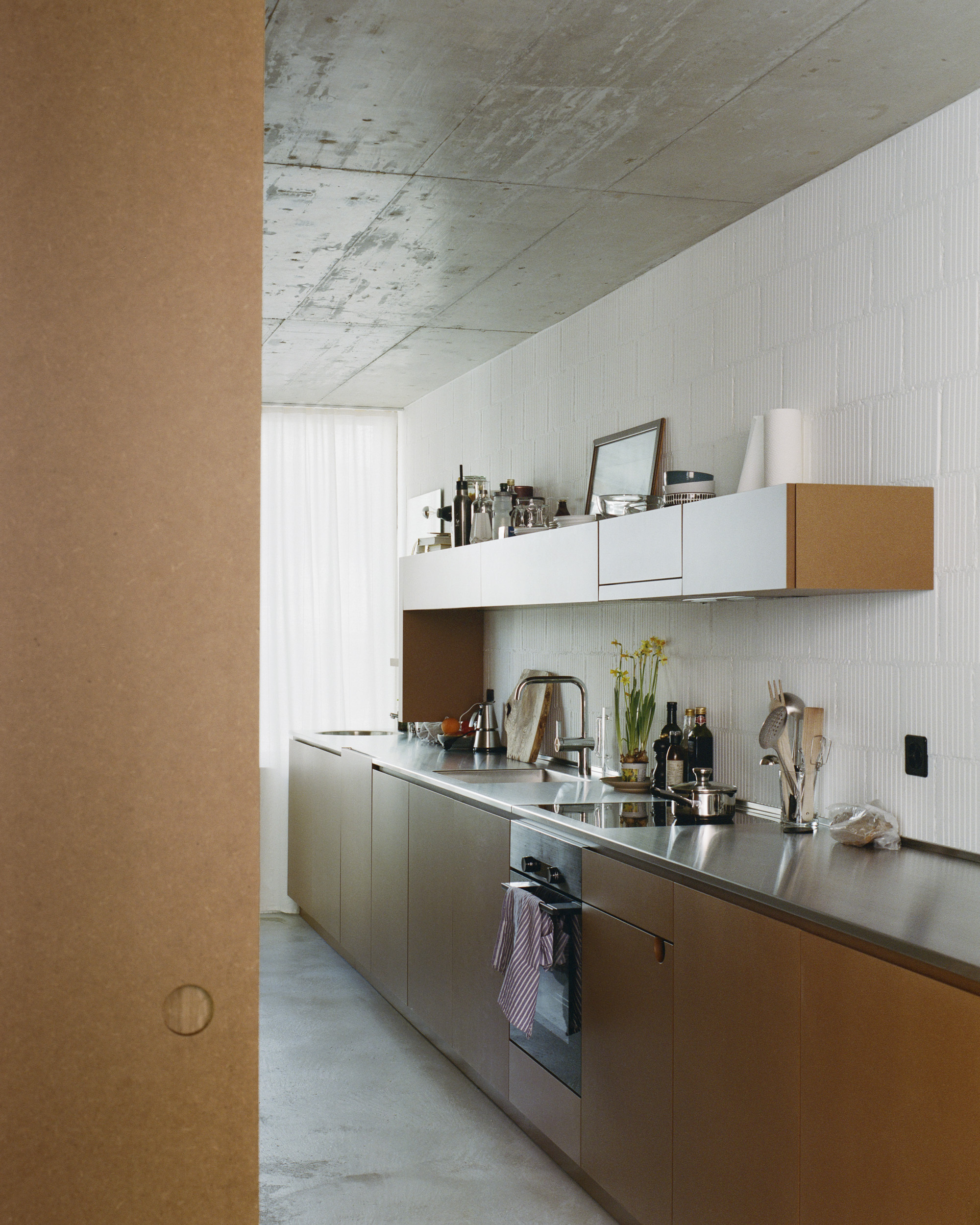 Galley kitchen with stainless steel countertops under an exposed concrete ceiling with daylight
